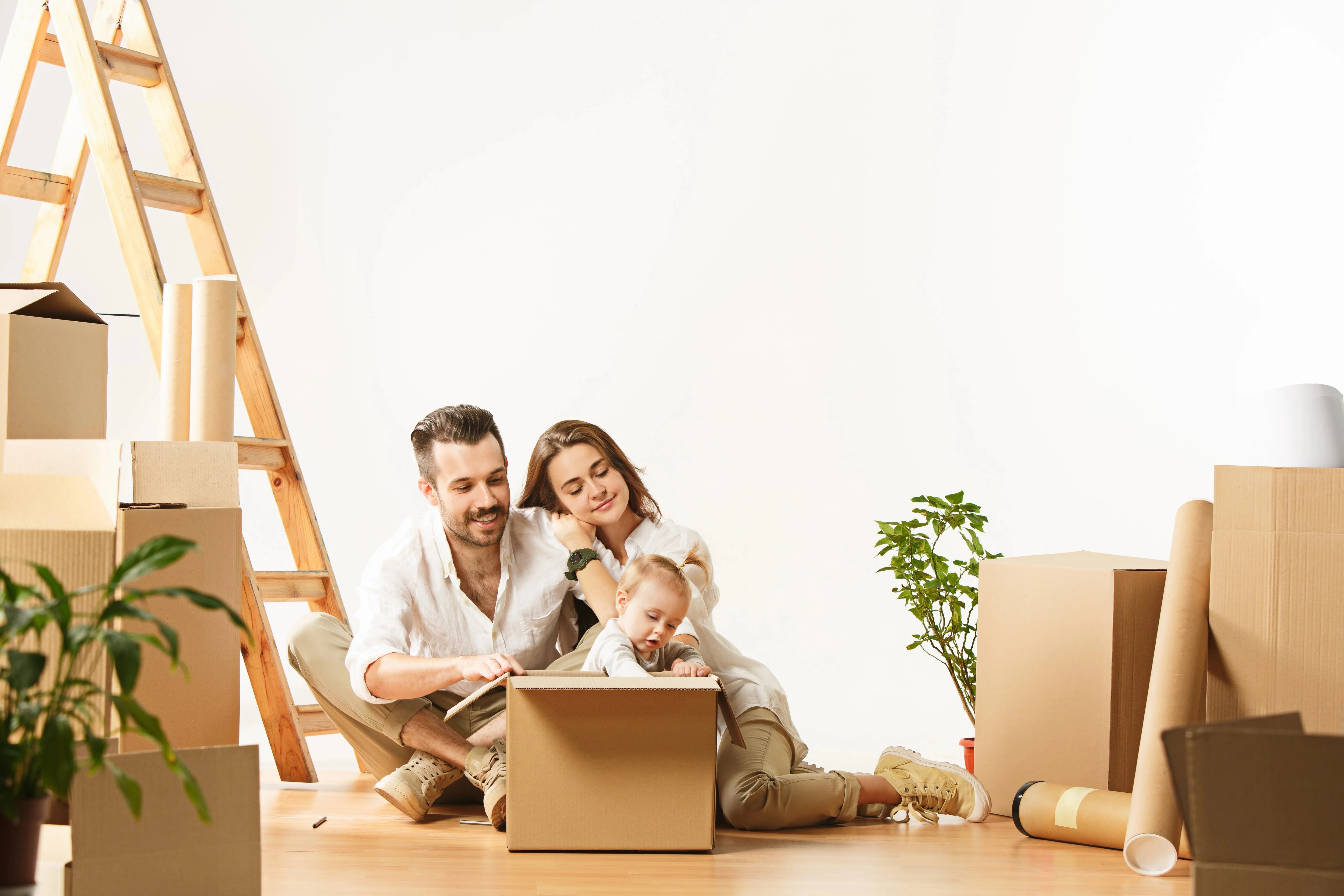 Husband, wife and young daughter sitting on floor surrounded by moving boxes while settling into new home.