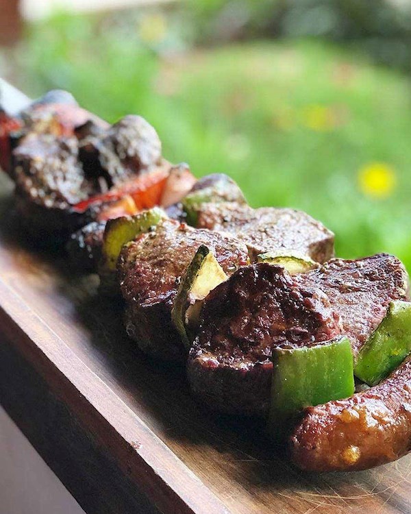 Four hands clinking beer glasses over table of food