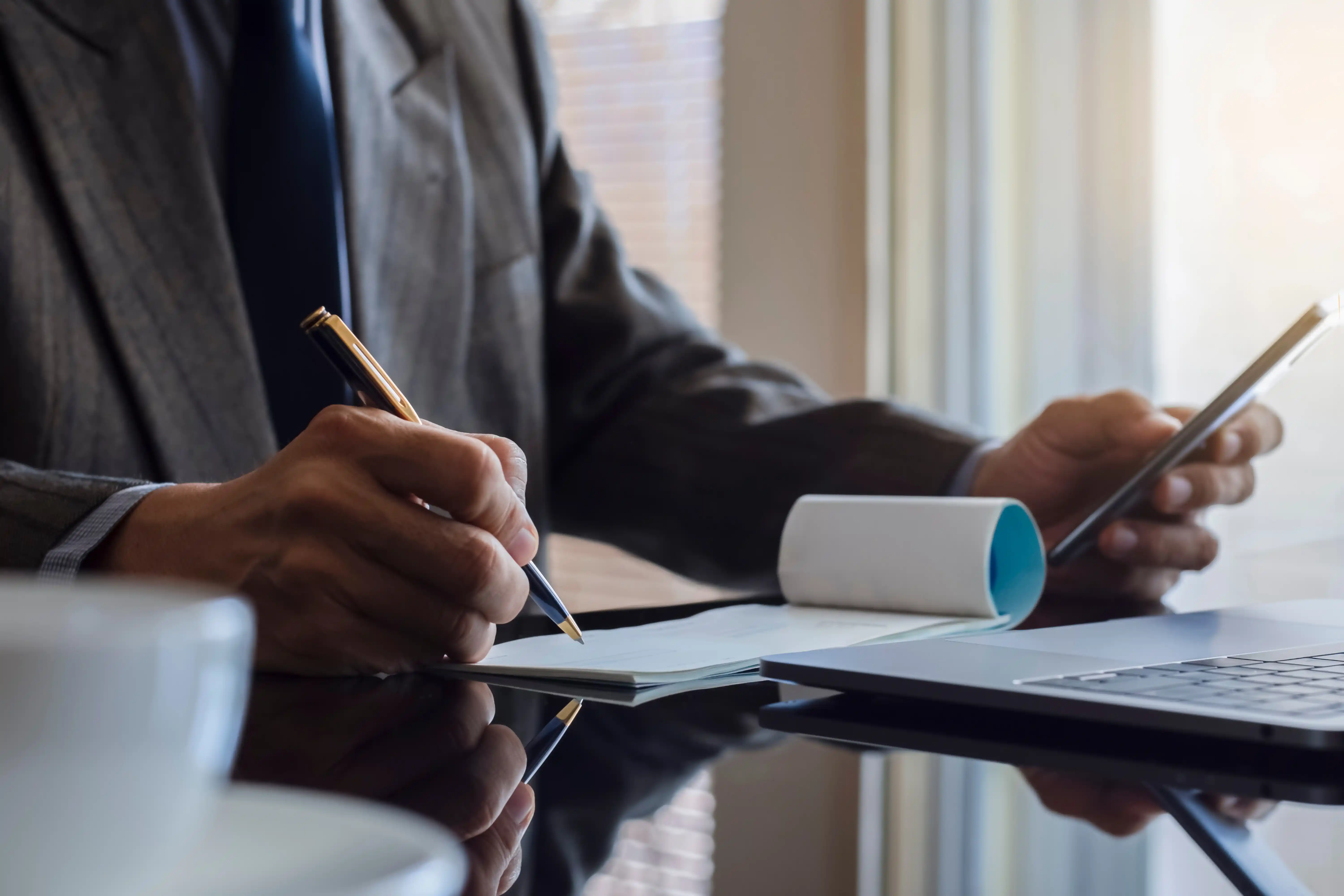 Close-up of a business professional writing a check at a desk next to a laptop, representing financial compensation, lost wages, and settlement recovery in a California disability discrimination claim