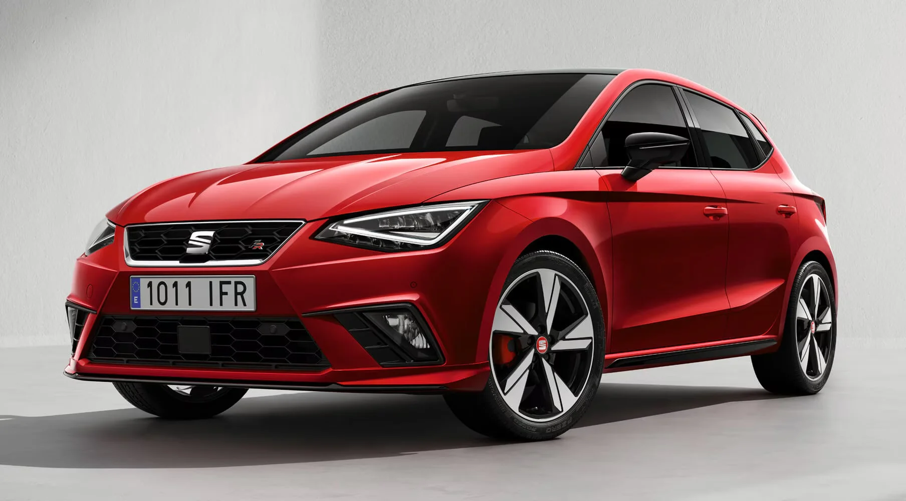 SEAT Ibiza FR rouge en prise de vue studio, présentant sa face avant agressive, ses optiques LED en forme de flèche et sa calandre noire sportive. Les jantes bi-ton, les lignes tendues et la posture basse soulignent le style moderne et énergique de cette version FR, symbole de la sportivité SEAT.