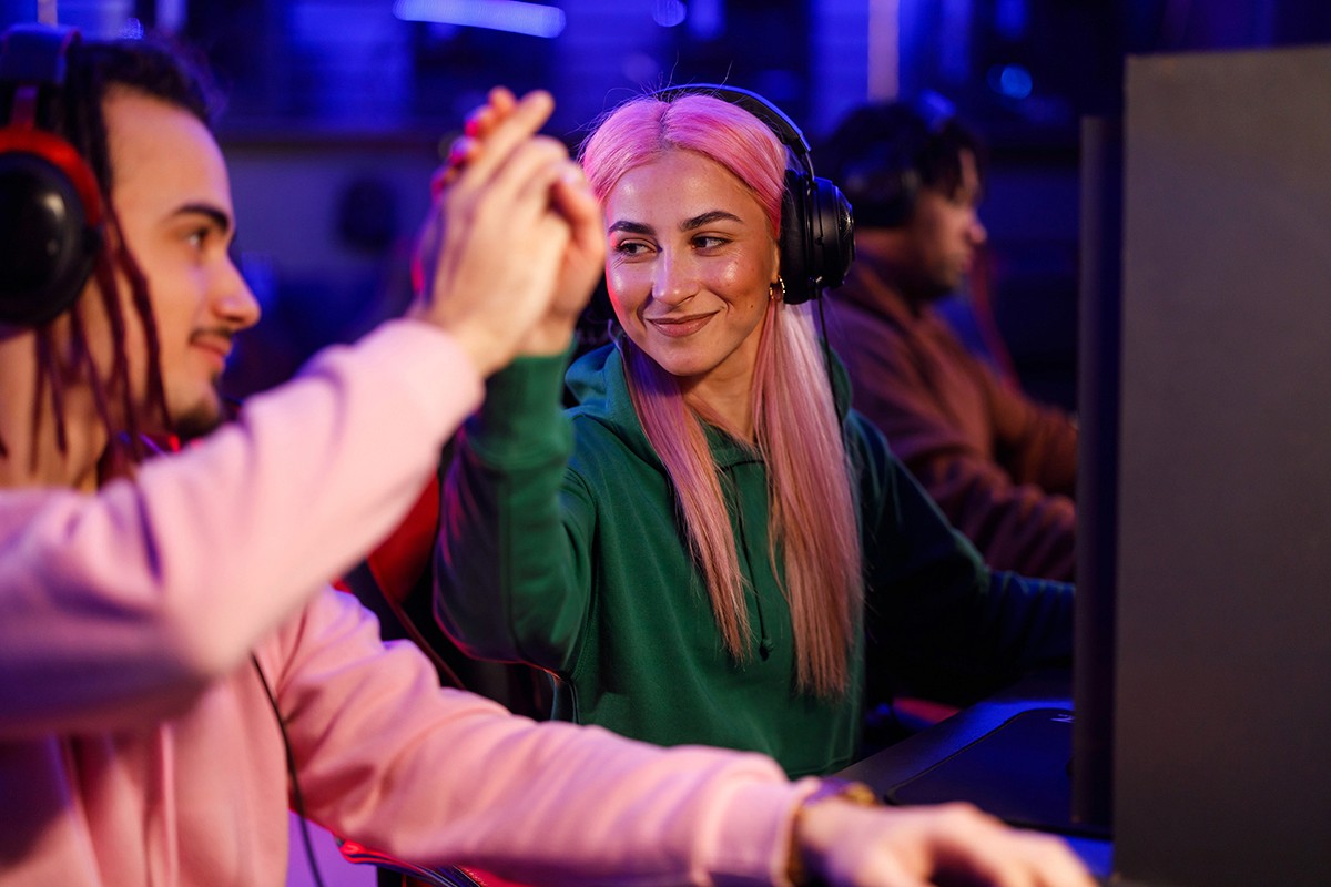 Two people seated at adjacent desks smile and high-five each other while wearing headsets, with others in the background focused on their screens