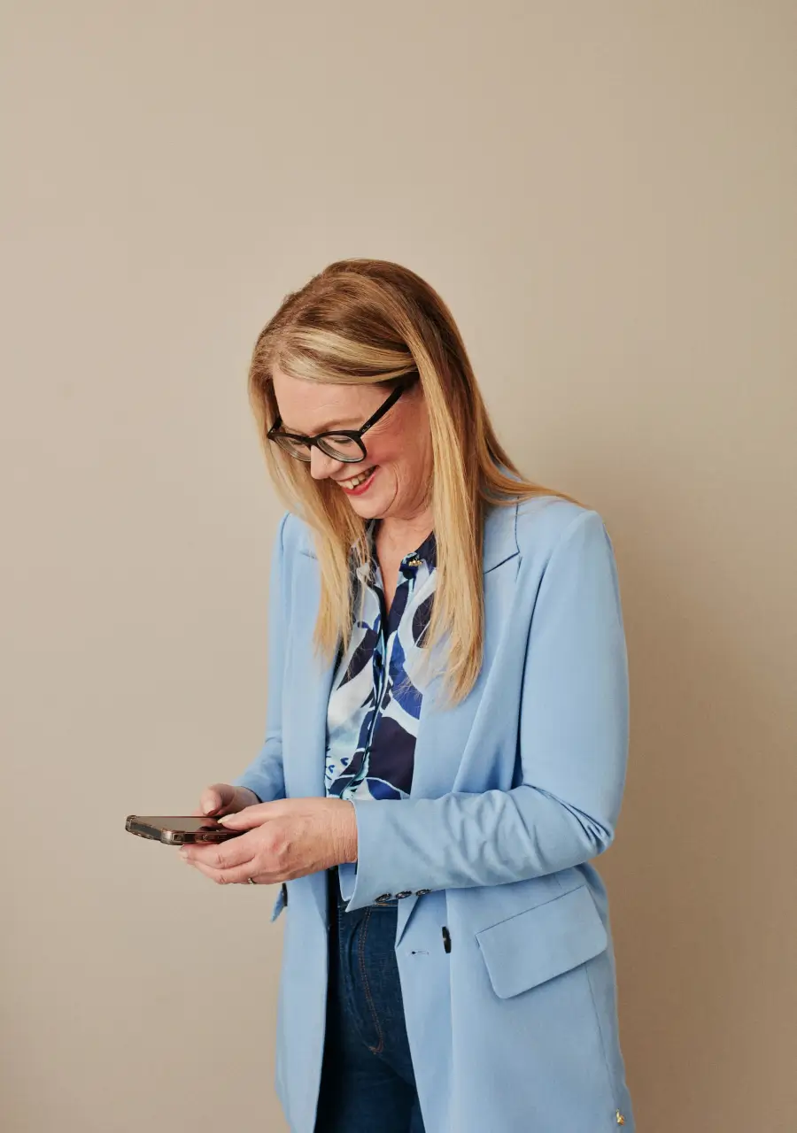 Photograph of a woman smiling, looking down at a smartphone in her hands