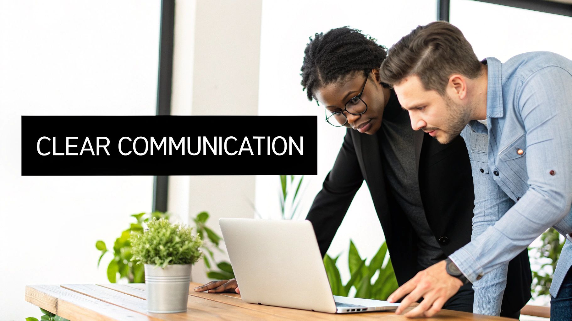 Two diverse colleagues collaborate on a laptop, demonstrating clear communication in a professional setting.