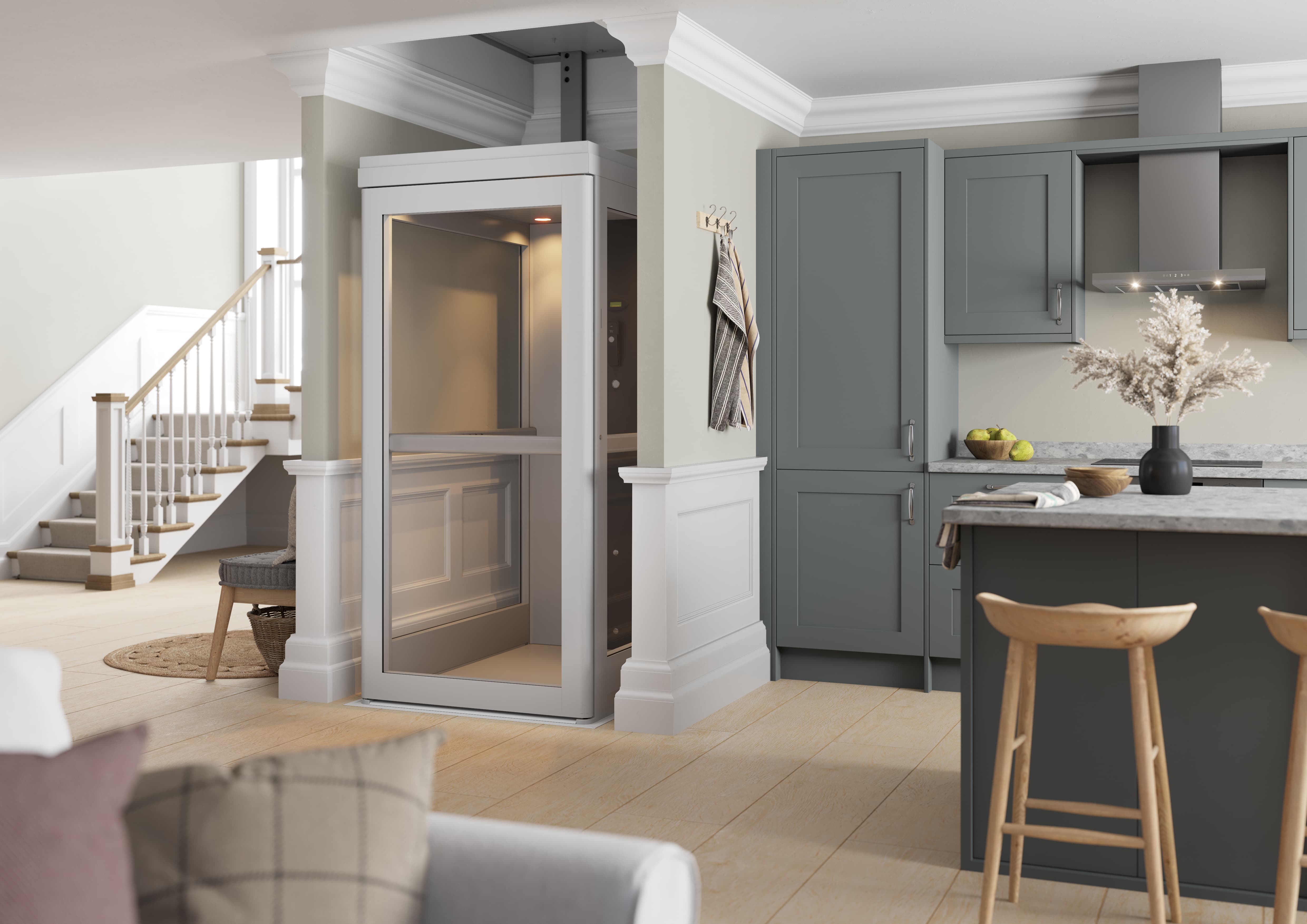 A white glazed through-floor home lift installed in a residential living room, with a fully enclosed cabin, control panel, and handrail visible, rising through the ceiling between floors.