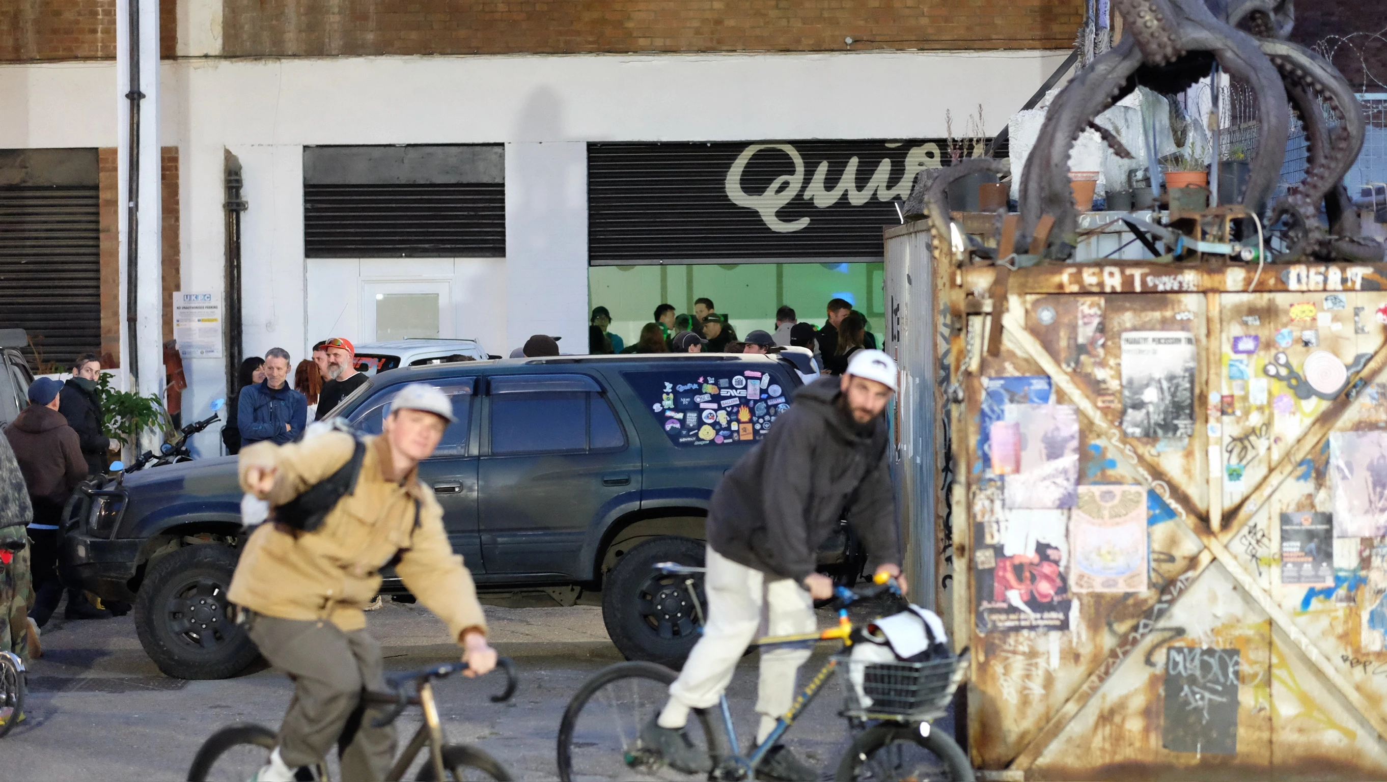 Rob Quirk sat in dark workshop in overalls, flicking though drawings. Light shines on large picture on wall and bike mounted behind him.