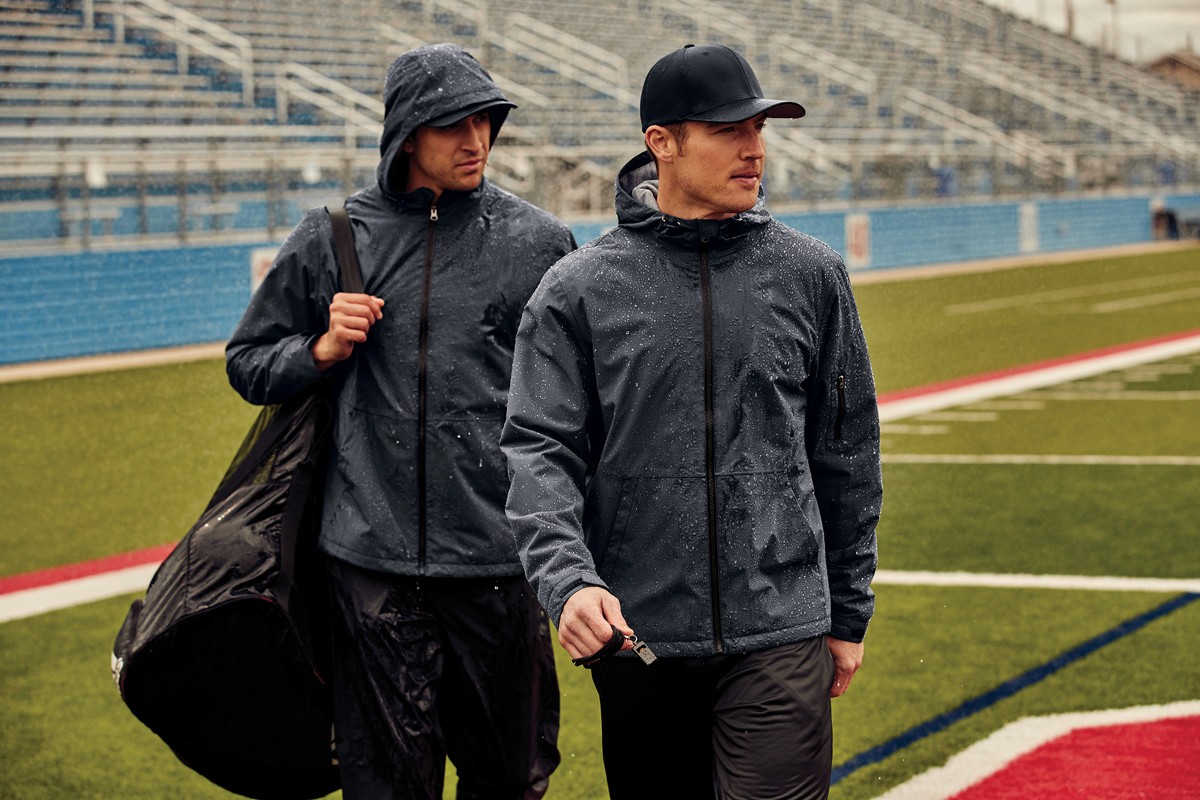 Two people wearing insulated jackeets that are a charcoal grey on an empty football field.