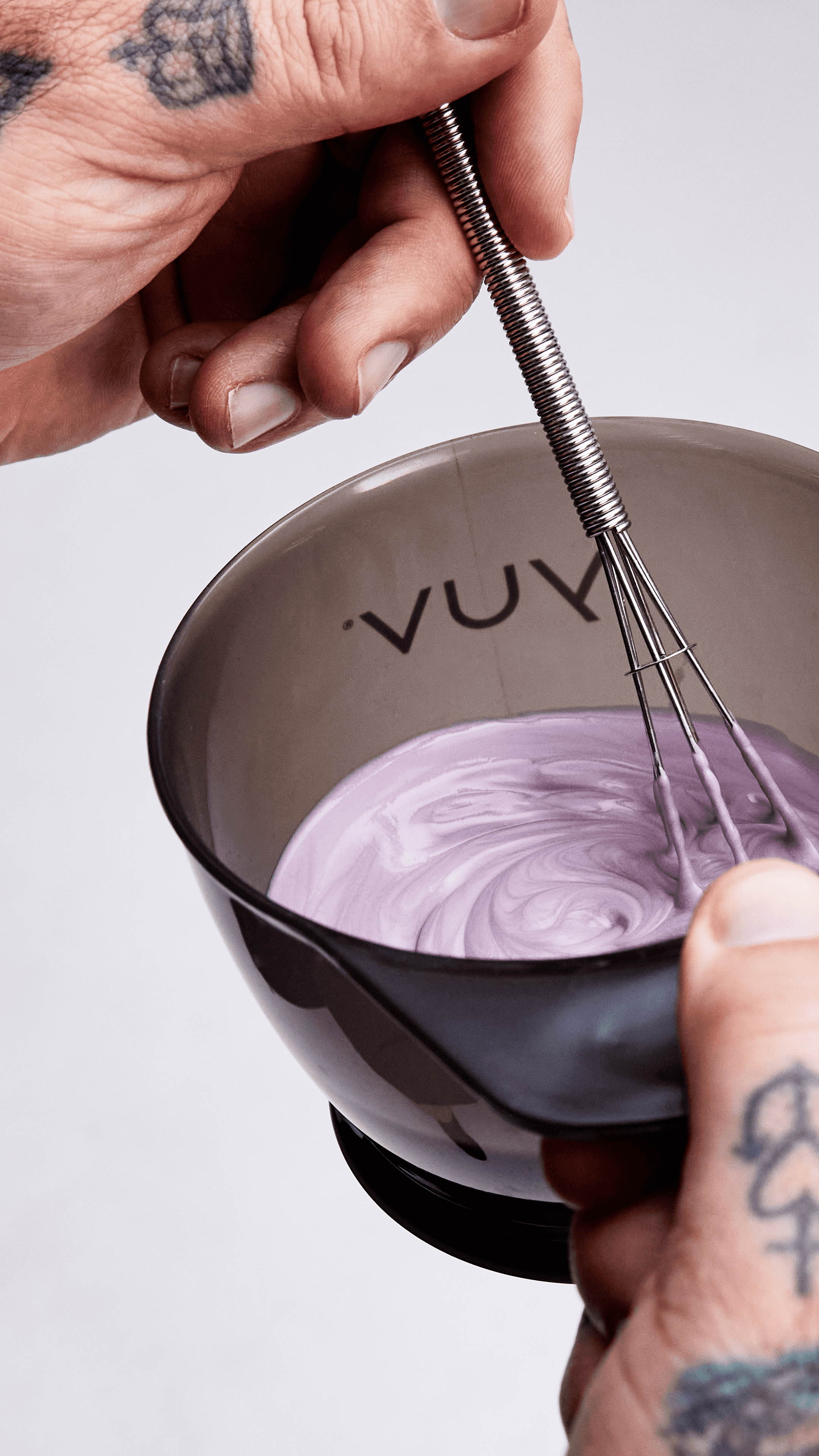 Hands holding a bowl of hair colour, using a whisk to mix the formula.