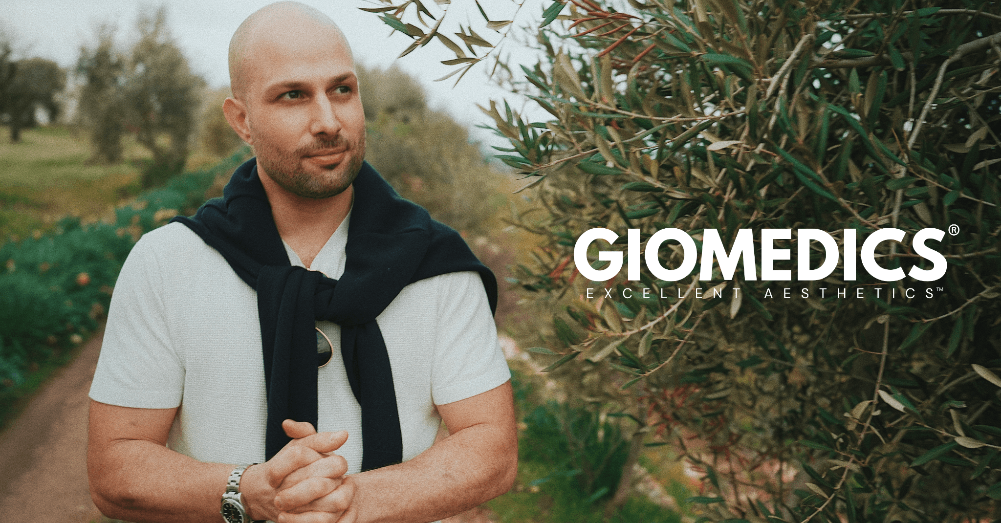 Man standing in olive grove, representing GIOMEDICS® physician-led European aesthetic medicine brand.