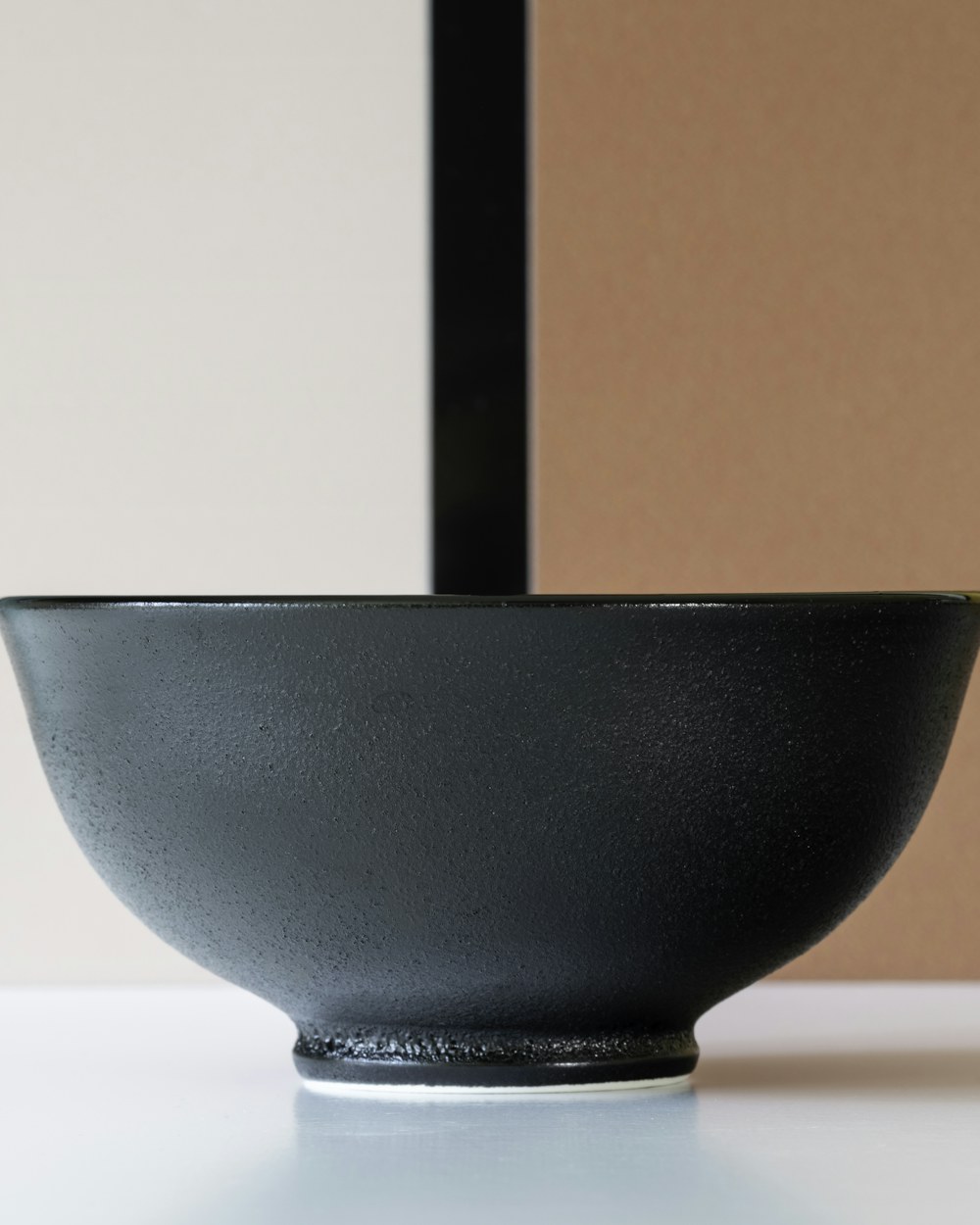 A deep black stoneware bowl against a two-tone tan and black ground