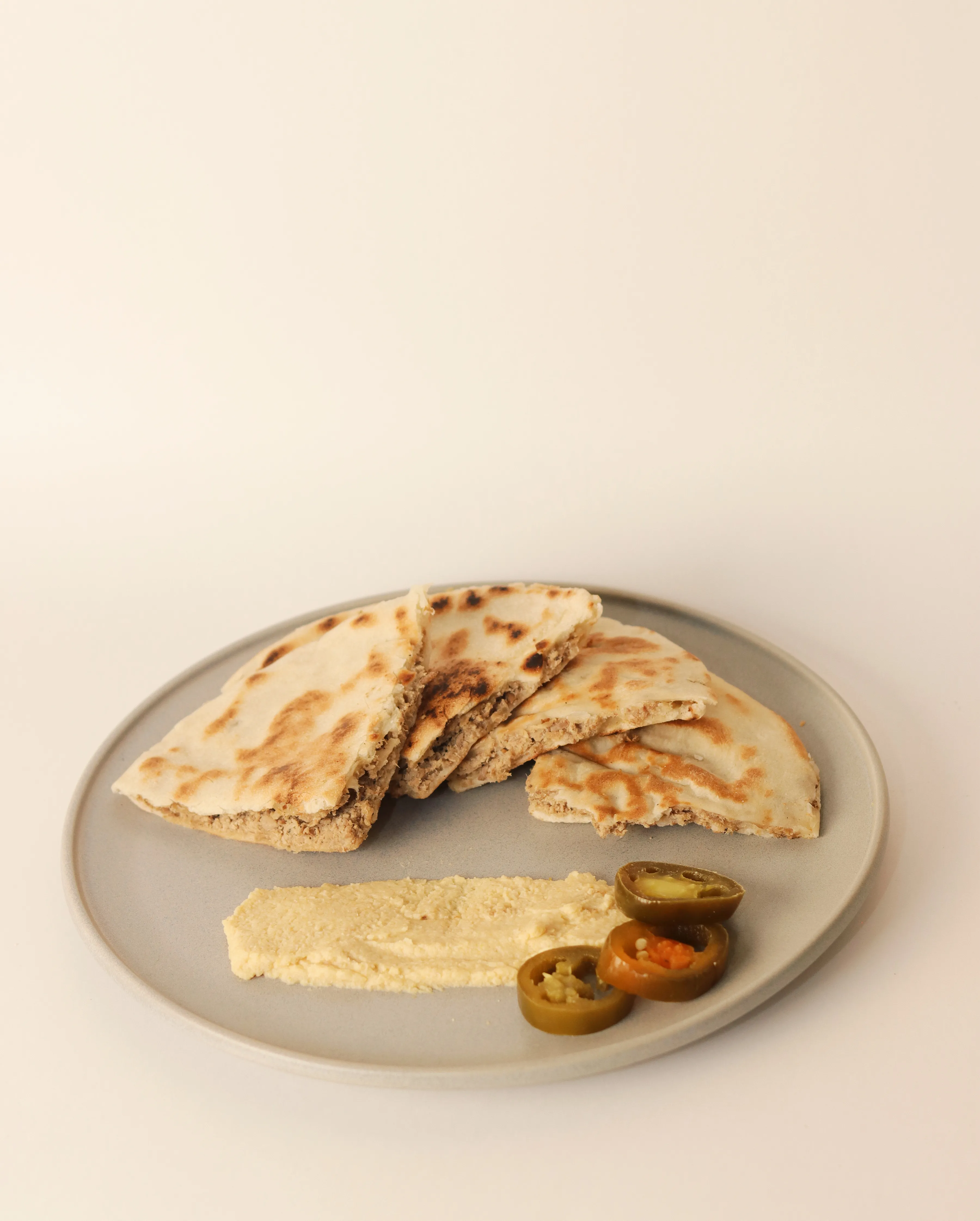 Pan libanés con hummus y chiles en plato gris.