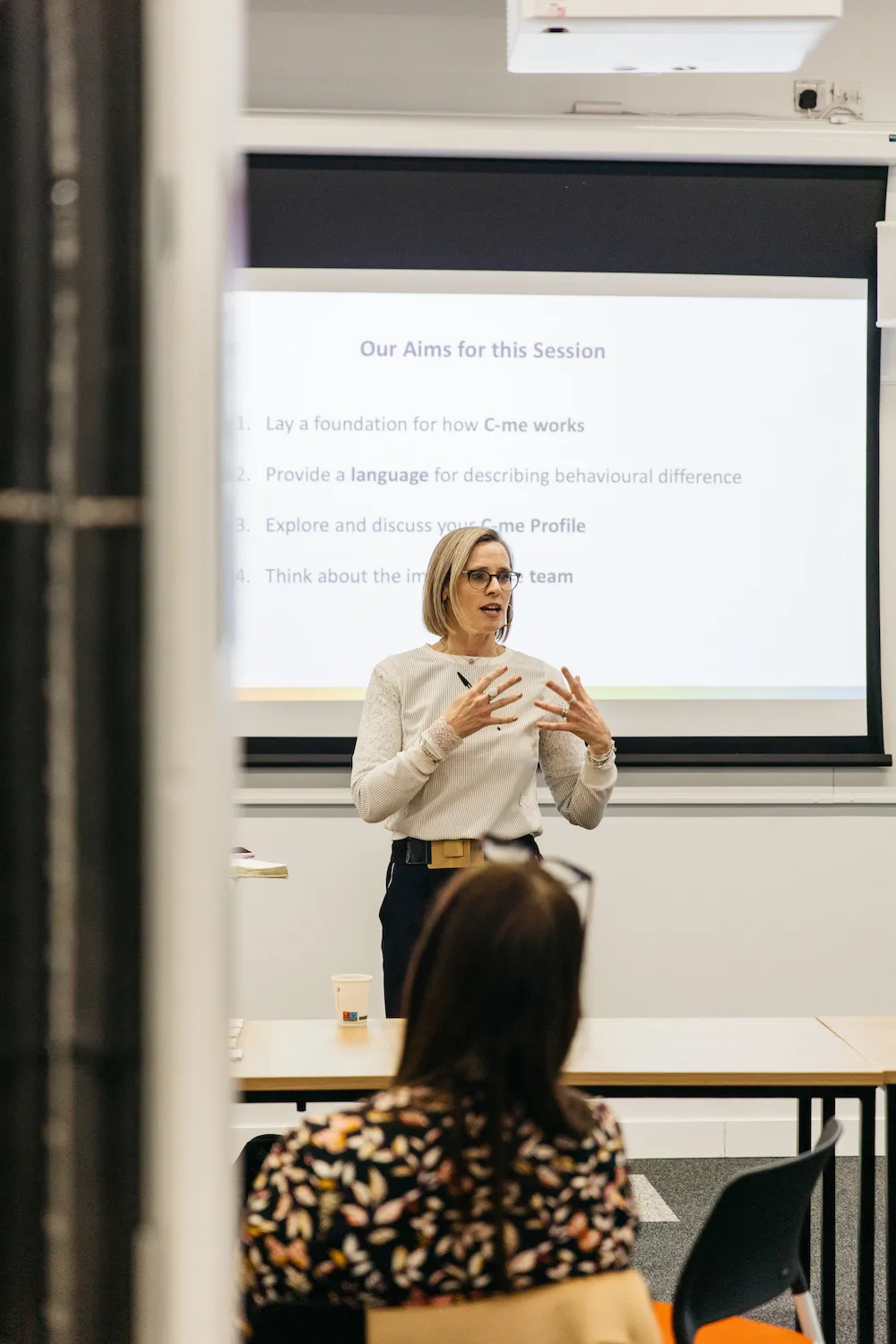 Person giving a lecture to an audience in front of the screen.