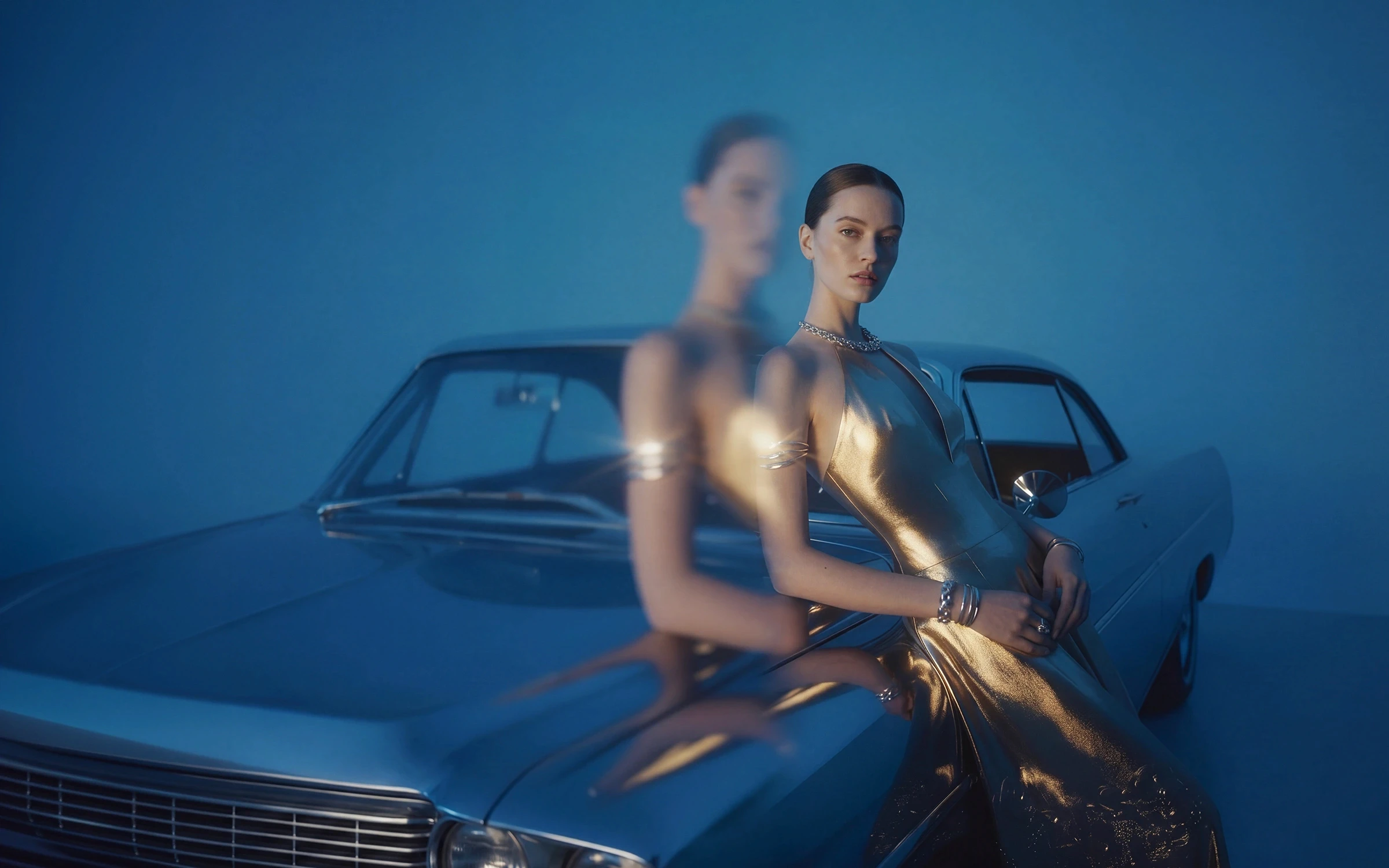 Woman in a metallic gold dress leaning on a classic silver car with a motion-blur double effect on a blue backdrop.