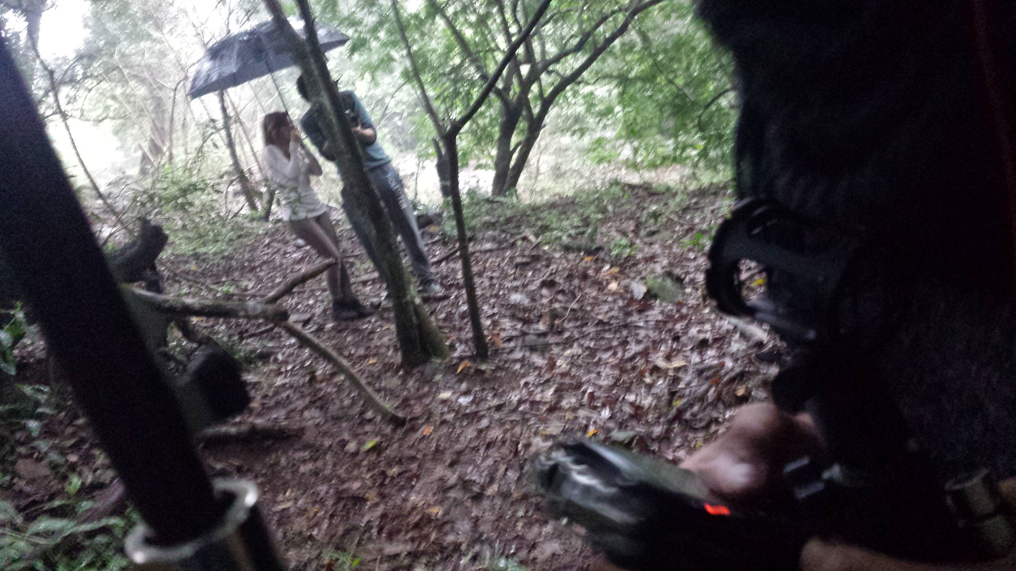 Pessoa de guarda-chuva na mata vista por trás da equipe com equipamento de filmagem