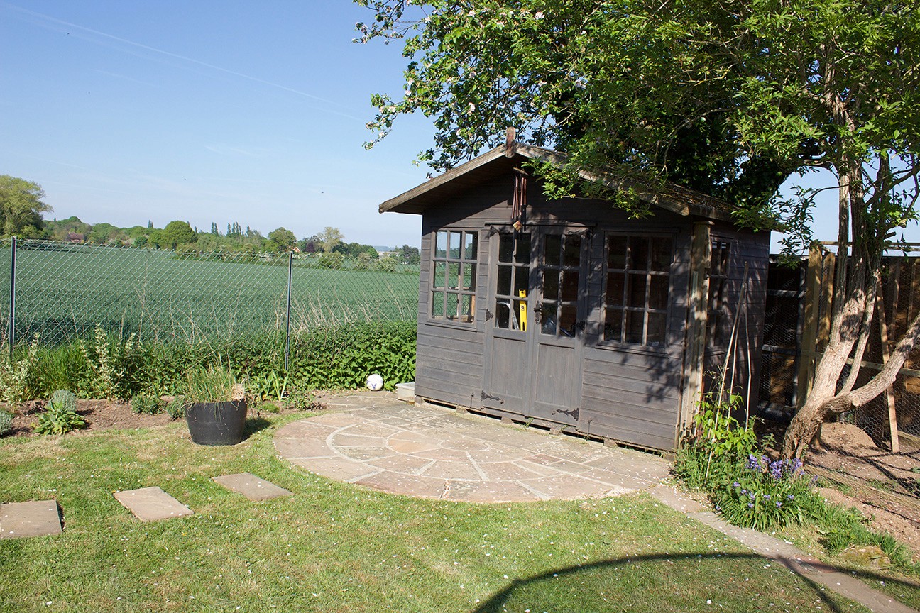 A small black shed surrounded by green grass and trees, with a clear blue sky in the background.