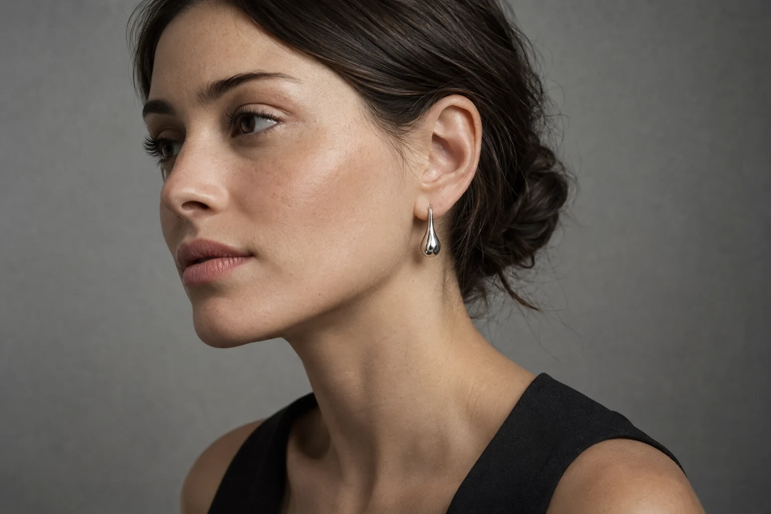Conceptual side-profile model crop with hair behind the ear and a clear silver earring sightline