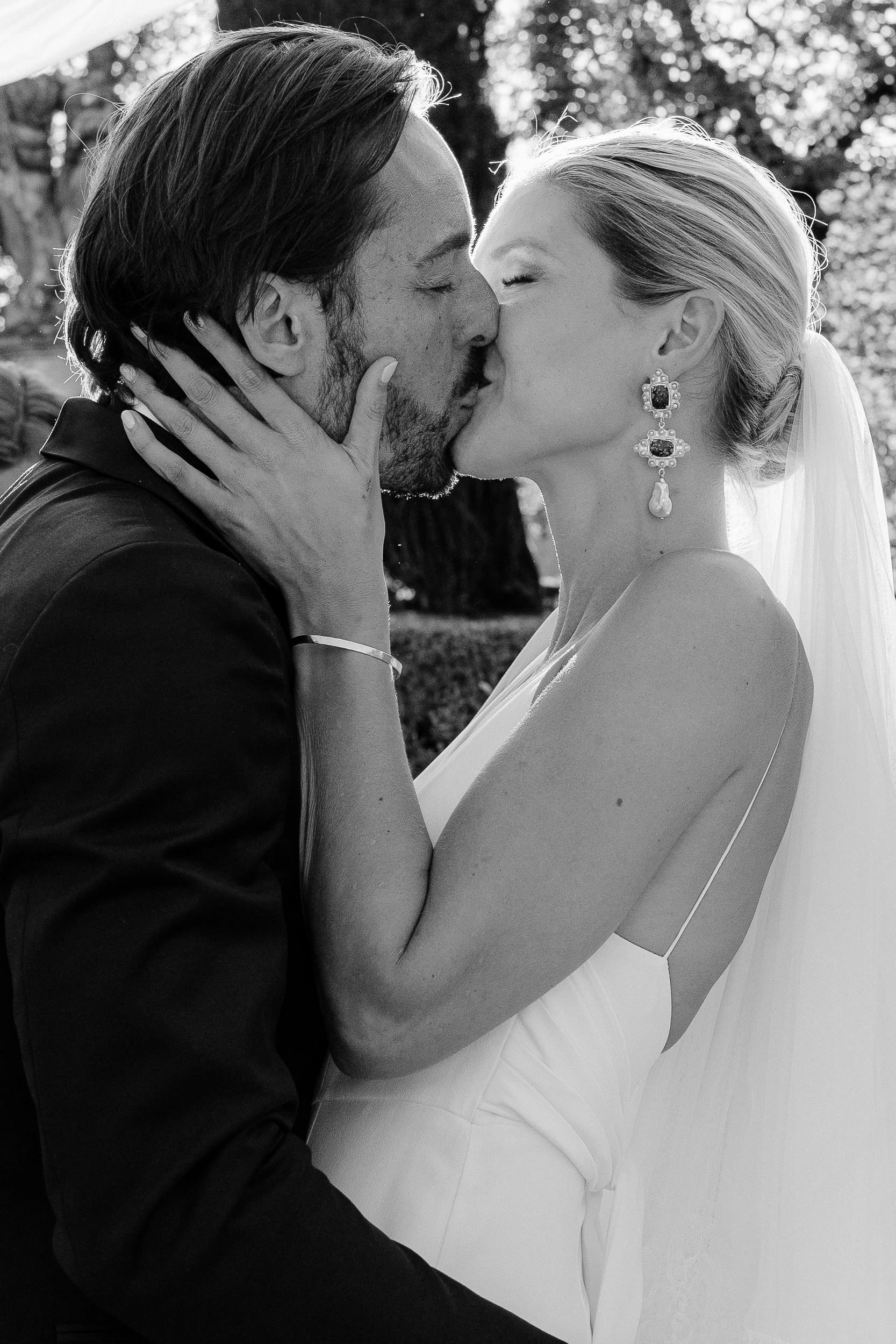A couple embraces and kisses during their wedding ceremony, captured in a black and white photo.