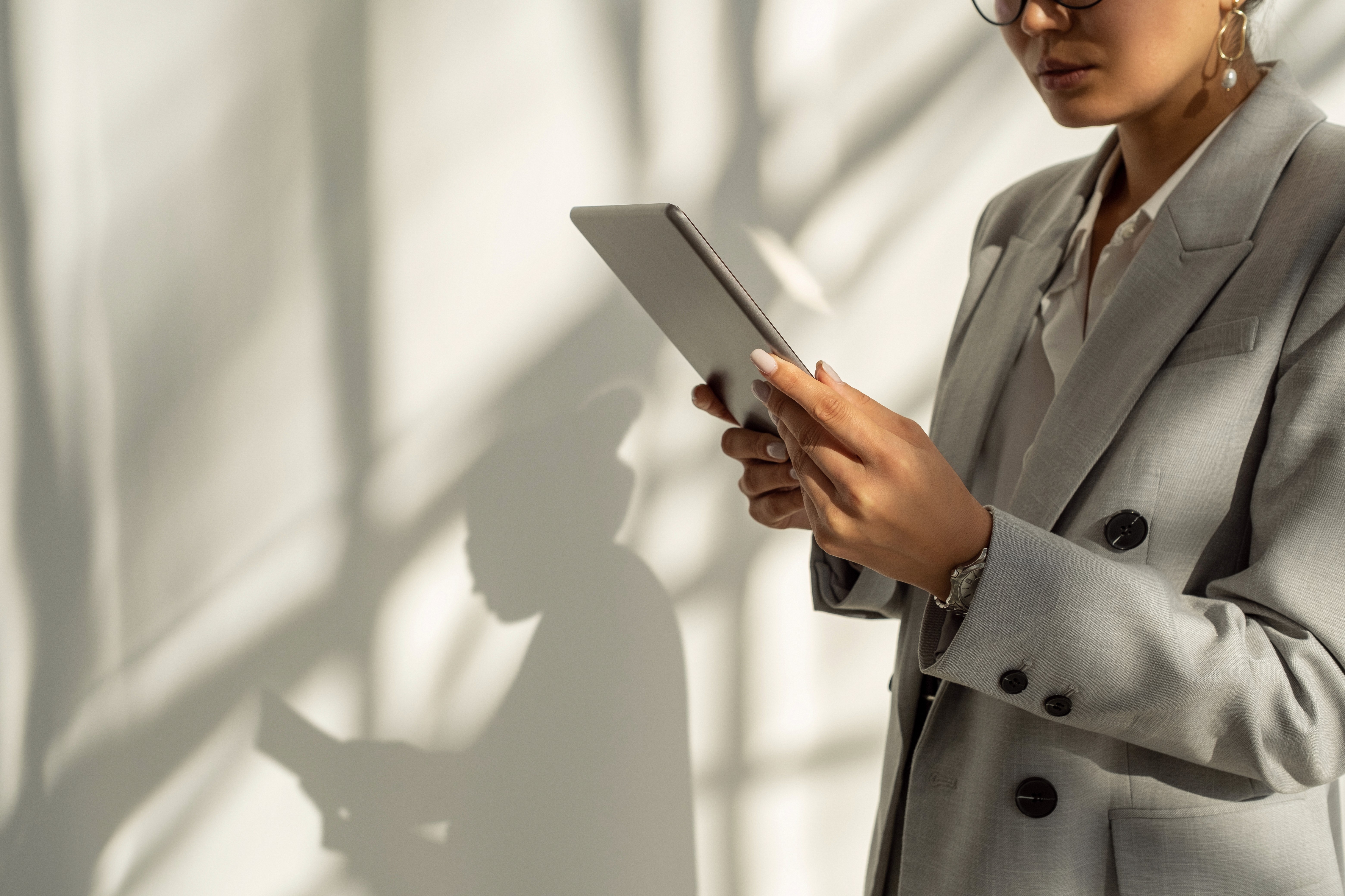 Businesswoman in a grey suit holding a tablet in a bright office environment.