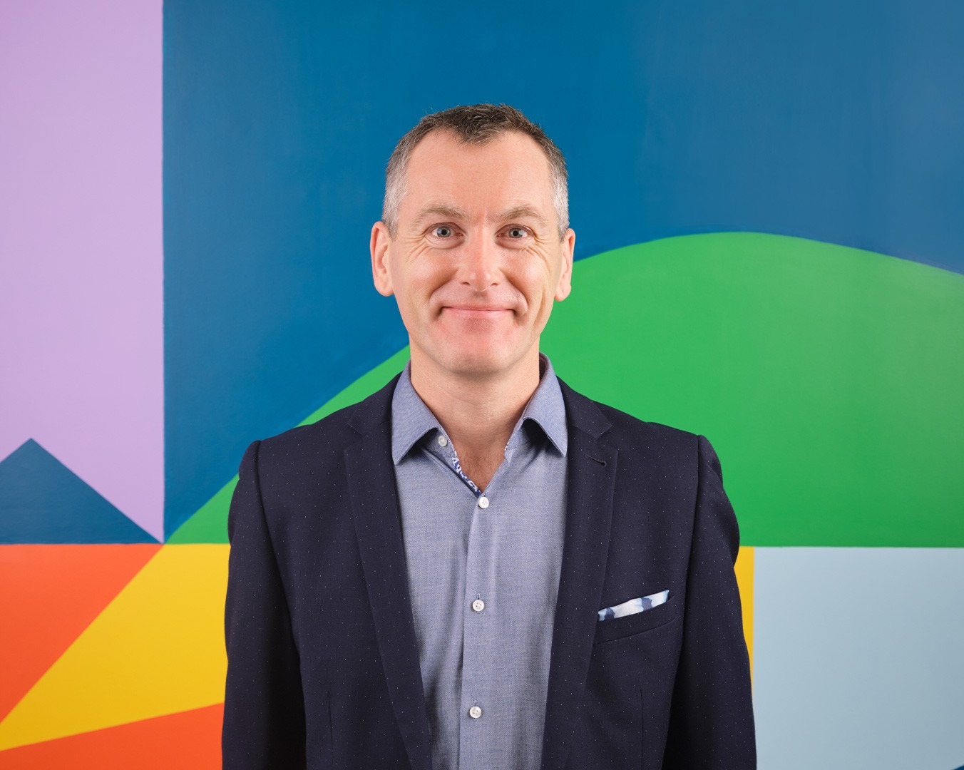Portrait of Tom Keogh standing in front of a colourful mural