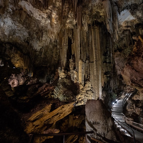 En svagt upplyst grotta med stalaktiter och stalagmiter, med en stig utrustad med räcken och belysning.