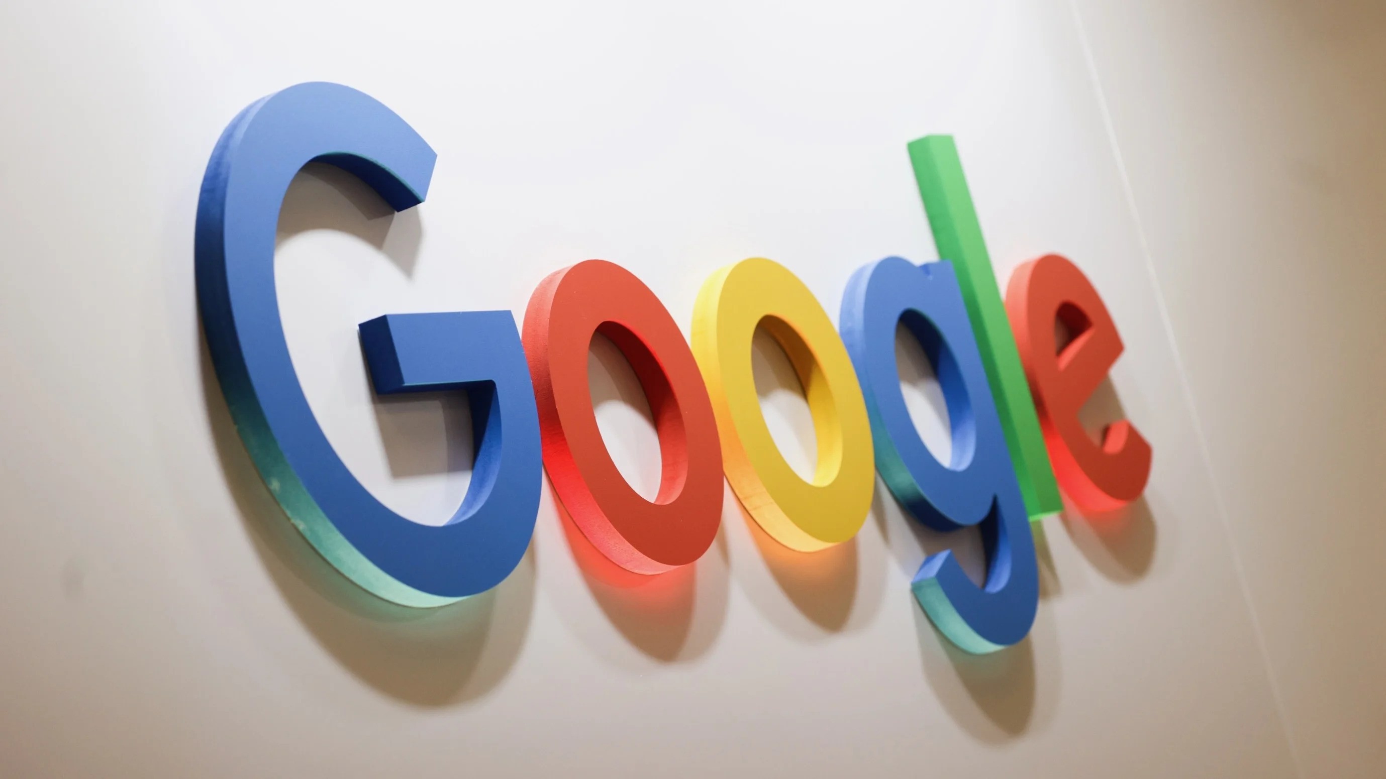 A colorful Google logo featuring blue, red, yellow, and green letters, displayed at a slight angle against a soft, off-white background.