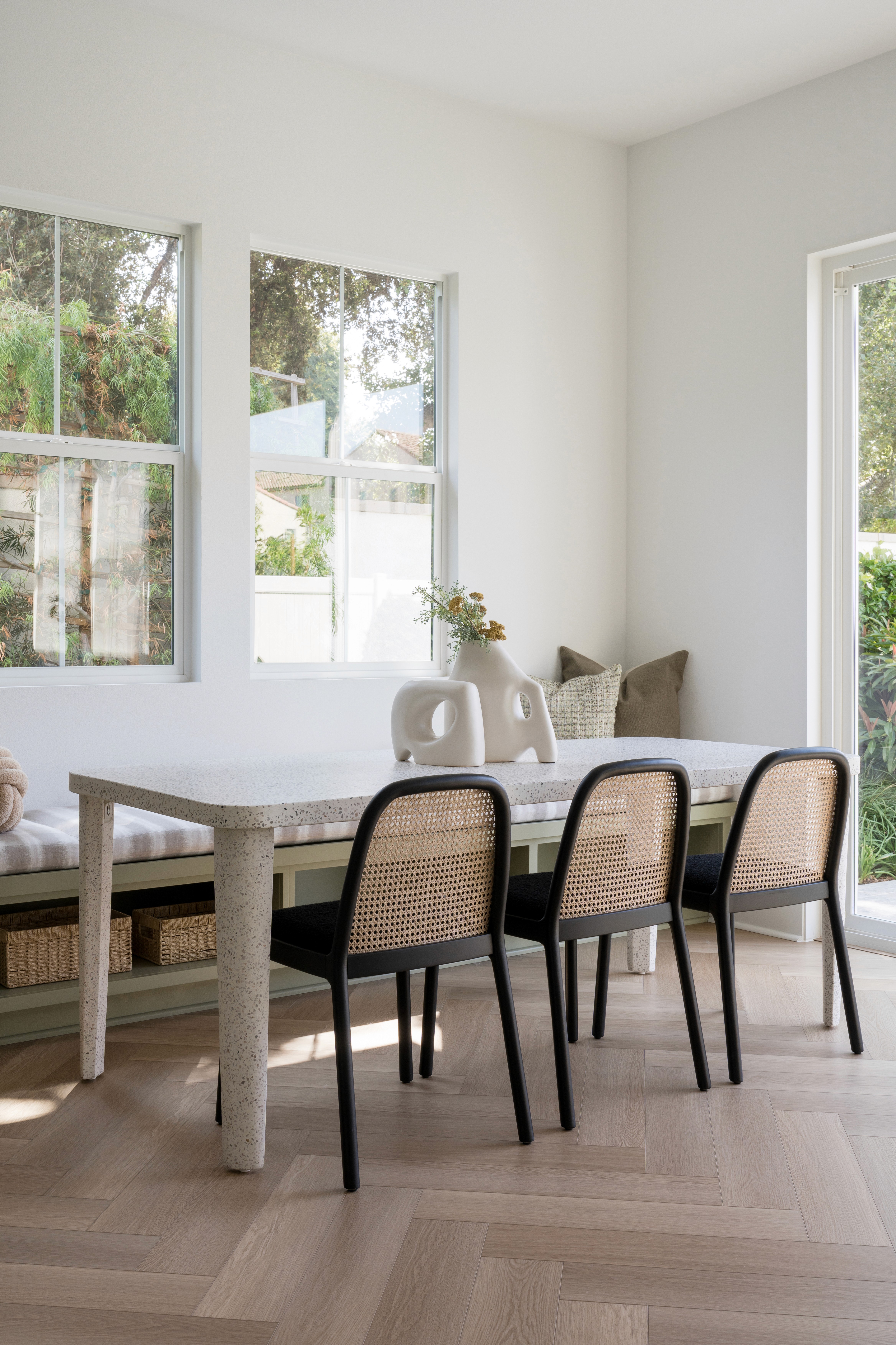 Open concept dining area with white travertine table, black and rattan dining chairs, sage colored built in bench seating with storage and grey and white cushion seating by Jubilee Interiors in Arcadia, California