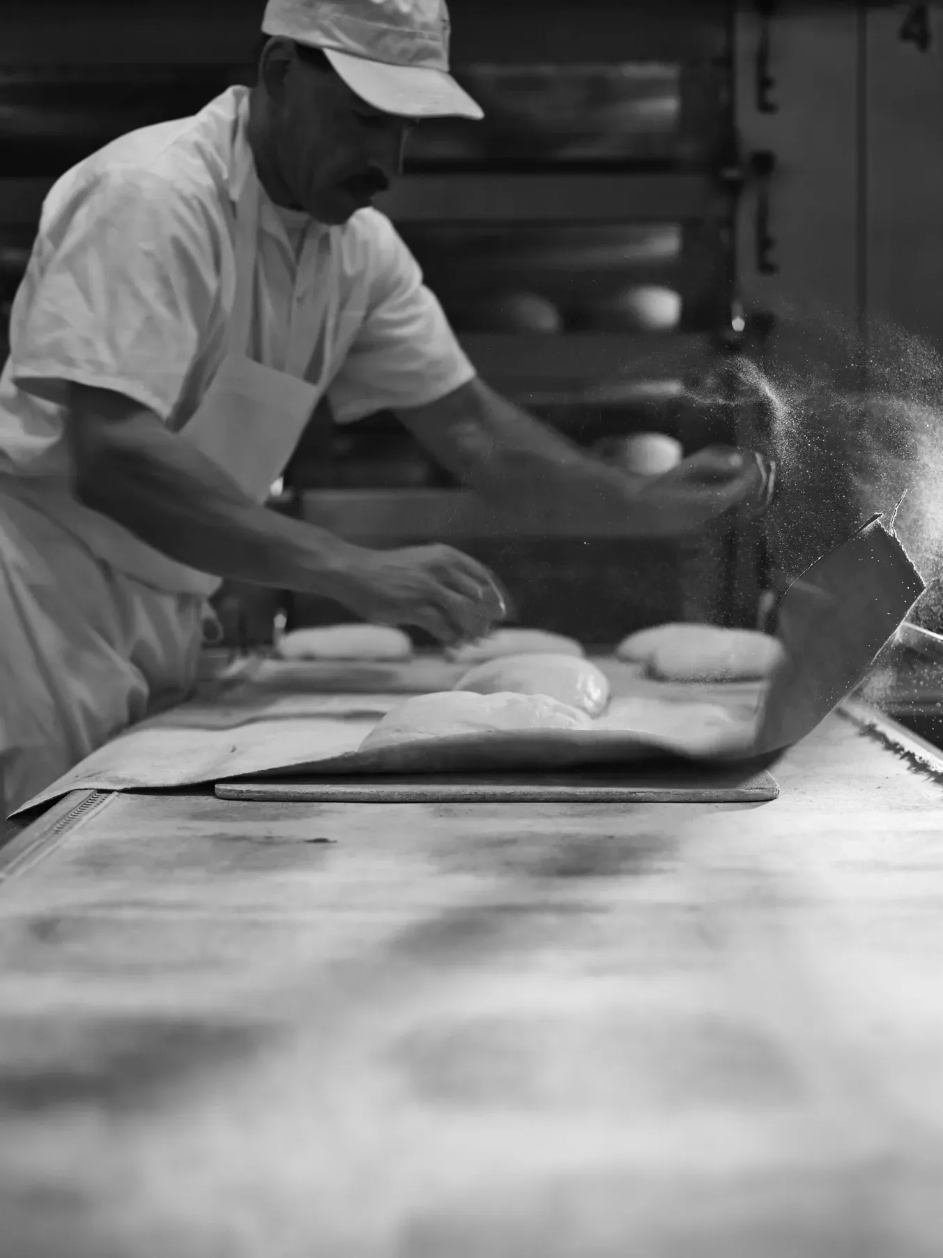 Baker preparing artisan bread dough with flour in a traditional bakery kitchen.