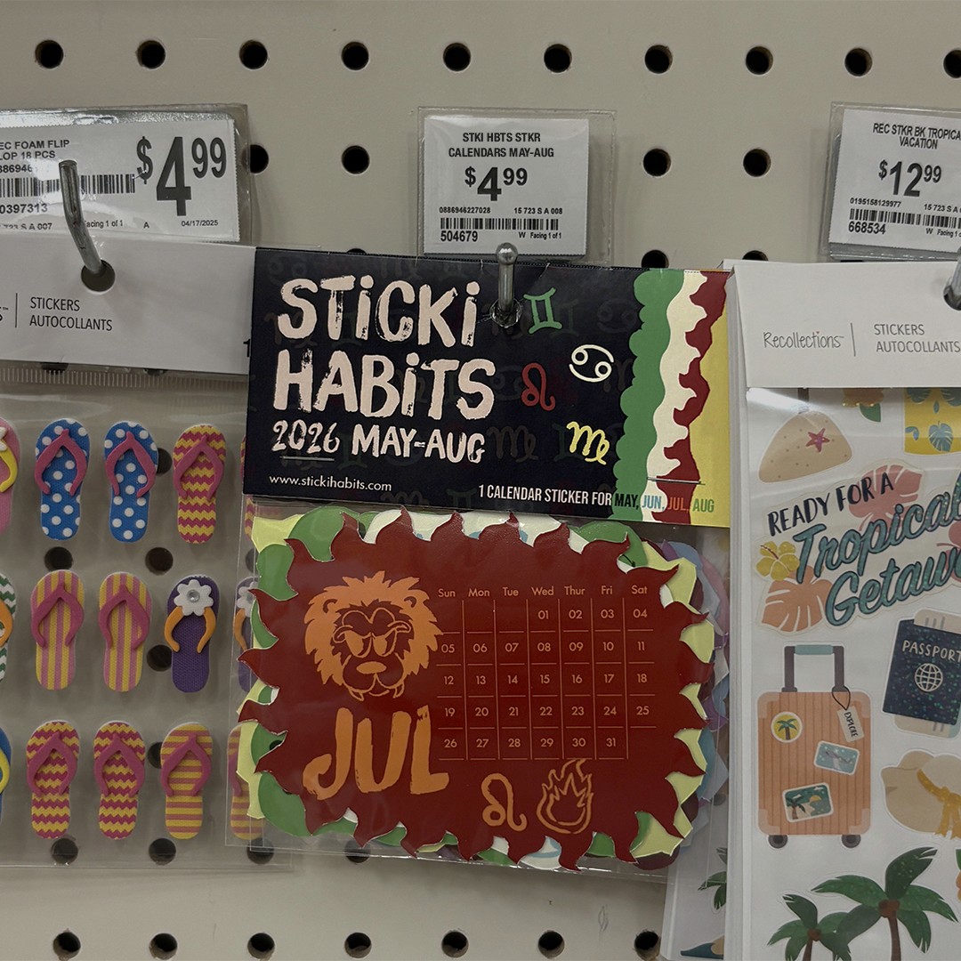 "Store display featuring 'Sticki Habits' 2026 calendar sticker priced at $4.99. The vibrant design includes a bold July motif with a lion and fire icon."