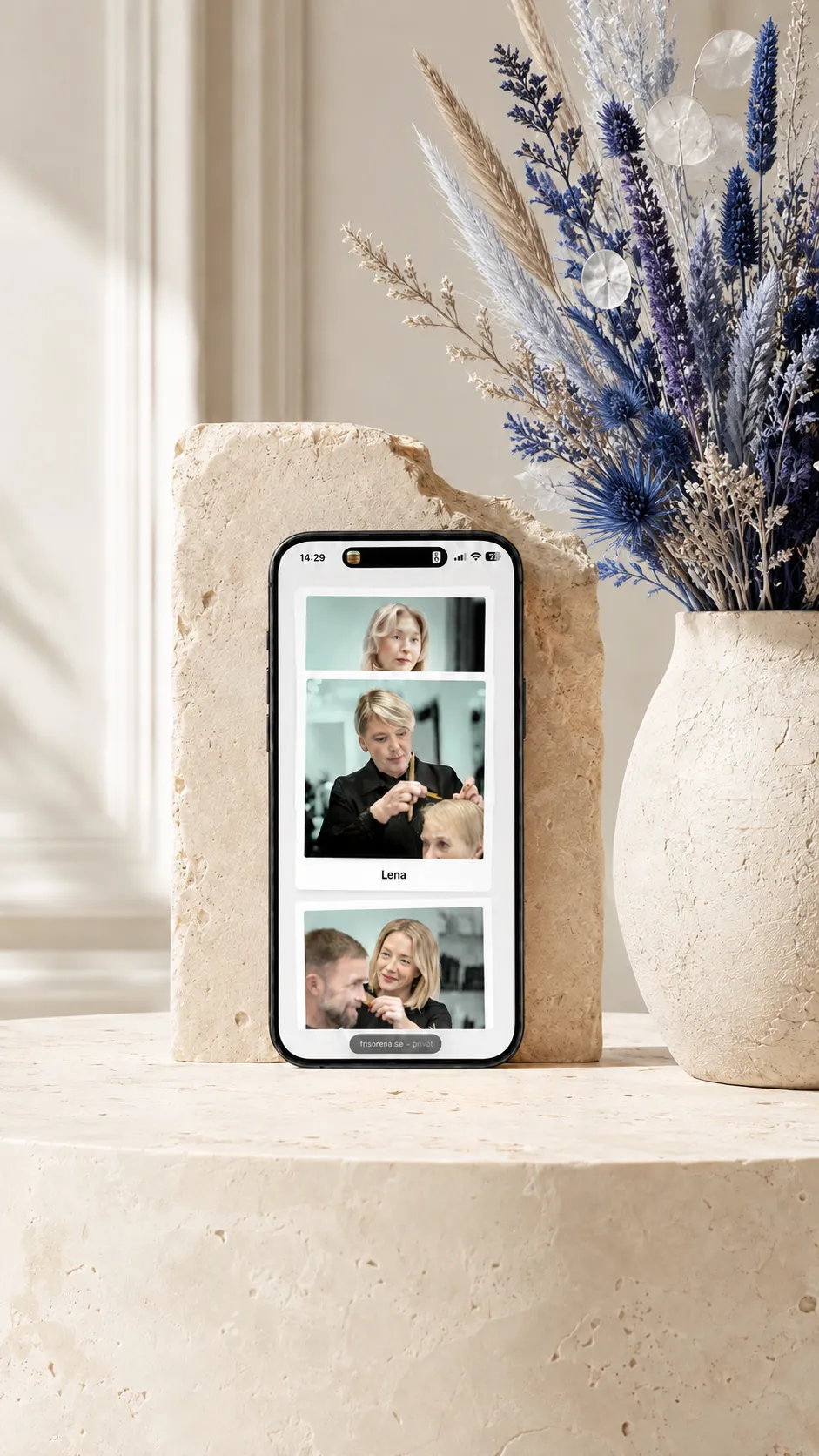 iPhone displaying the Frisörerna team page, styled with blue and lavender dried flowers beside a travertine stone support.