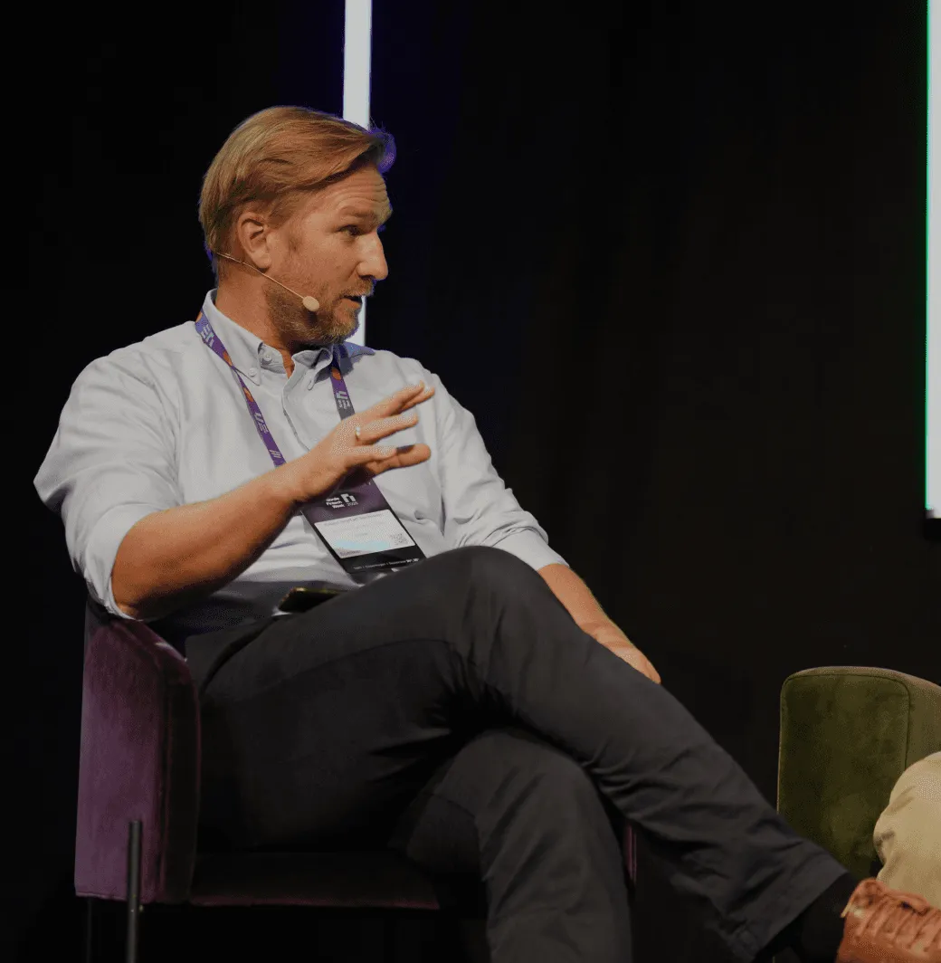 A person sitting on a stage holding a microphone, engaged in discussion at an event.