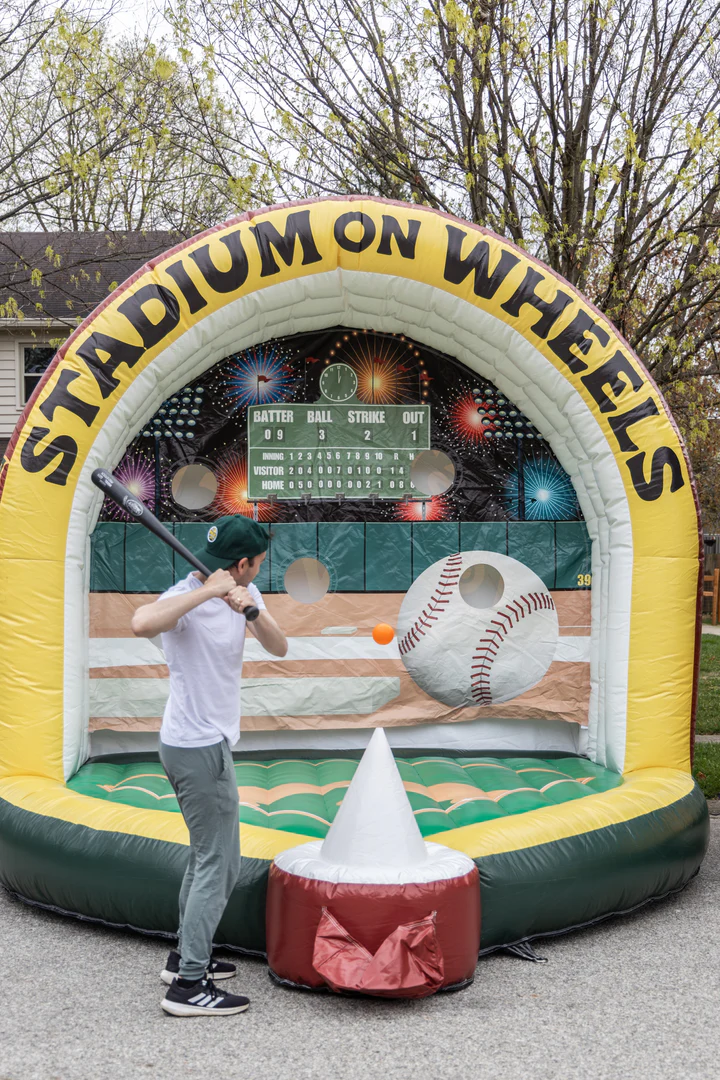 Someone hitting a ball with a baseball bat into an inflatable baseball game.