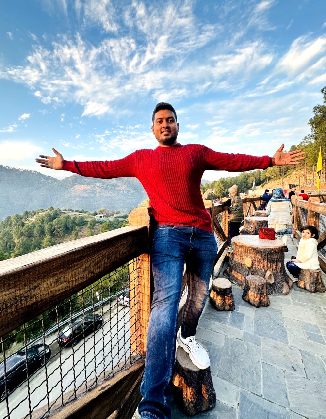 Basit in red sweatshirt standing on a balcony