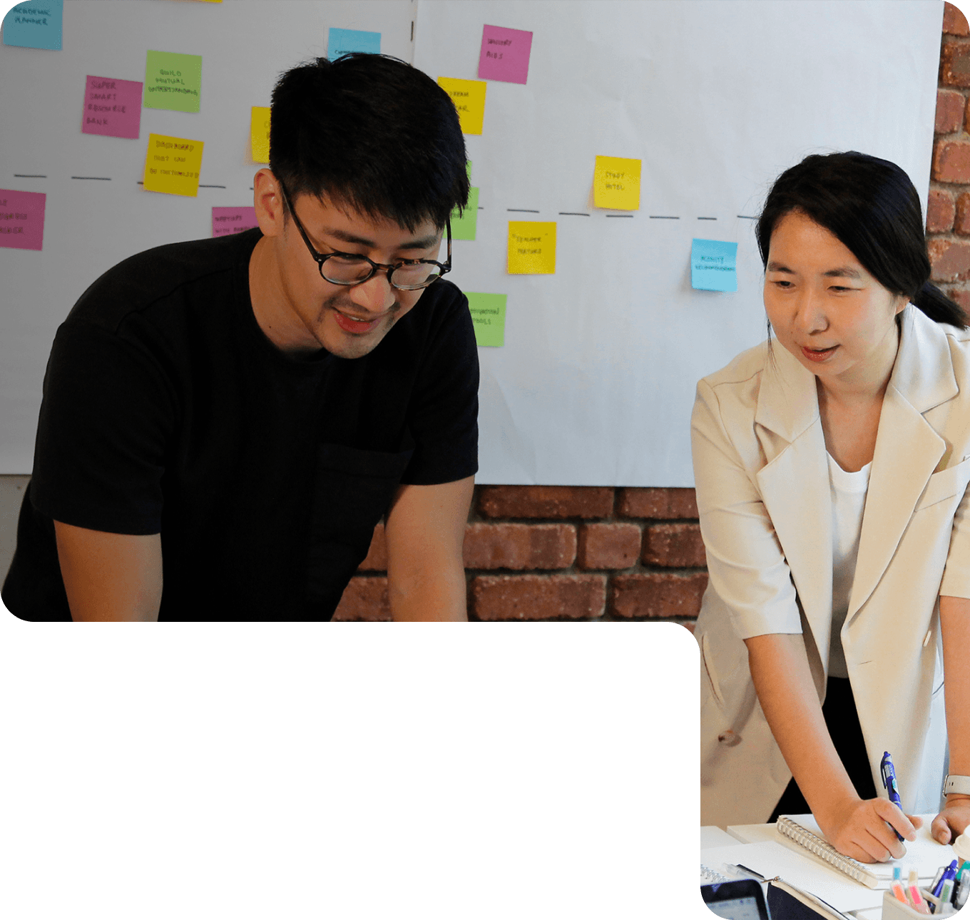 Two members of 55 Minutes collaborating in a modern workspace, discussing ideas in front of a laptop and a board with sticky notes.