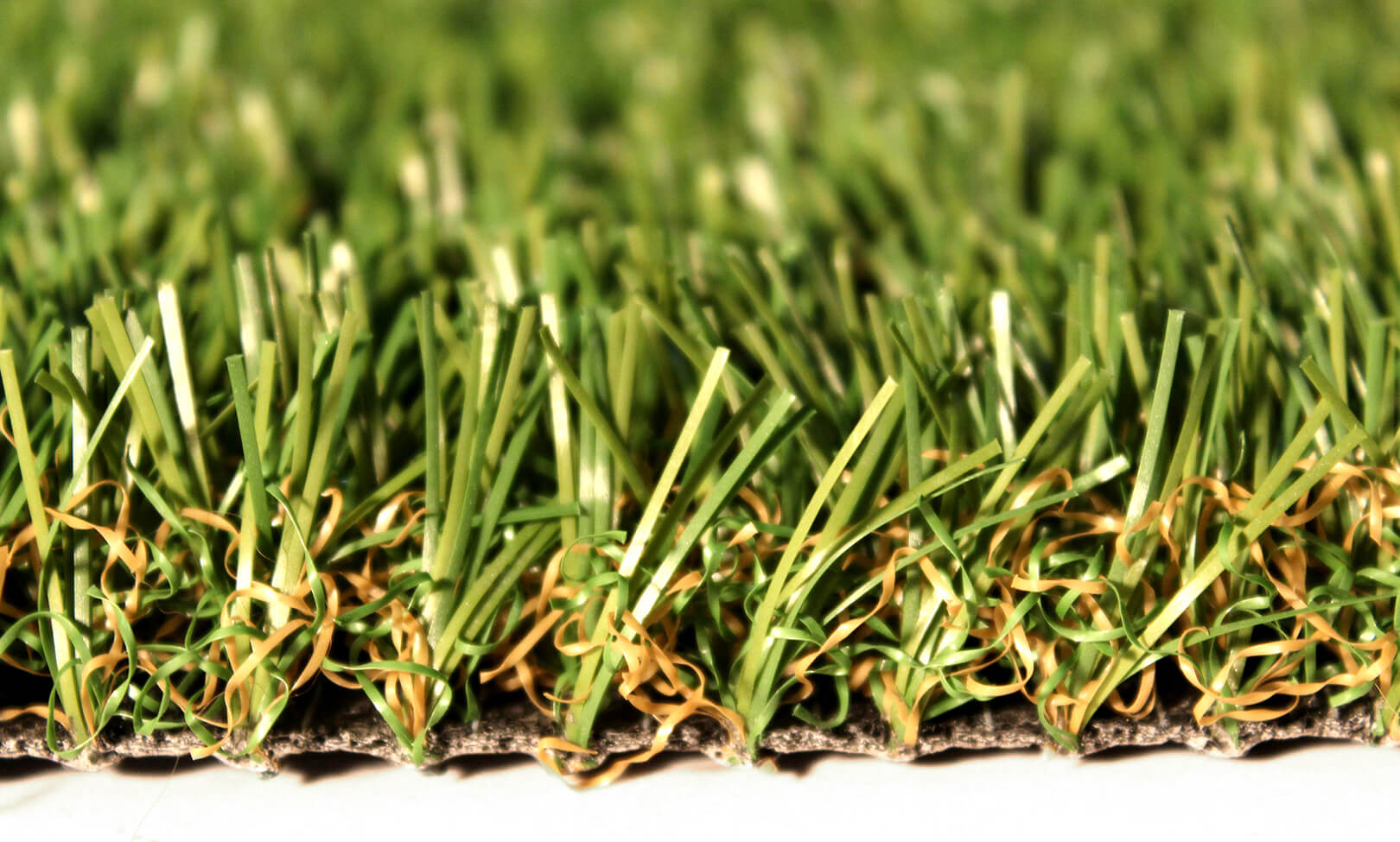 This is a close-up image displaying the intricately wound orange and green fibers of artificial grass within AGL Grass North's Kent Fringe grass.