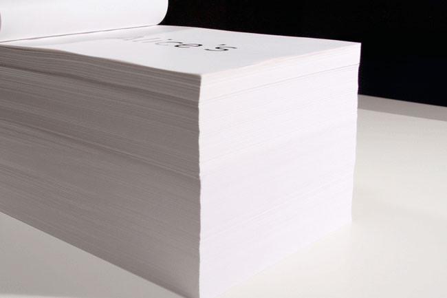 A stack of white paper sheets rests on a white surface. The top sheet displays the word “Alice’s” in black text. The stack is positioned against a black background.