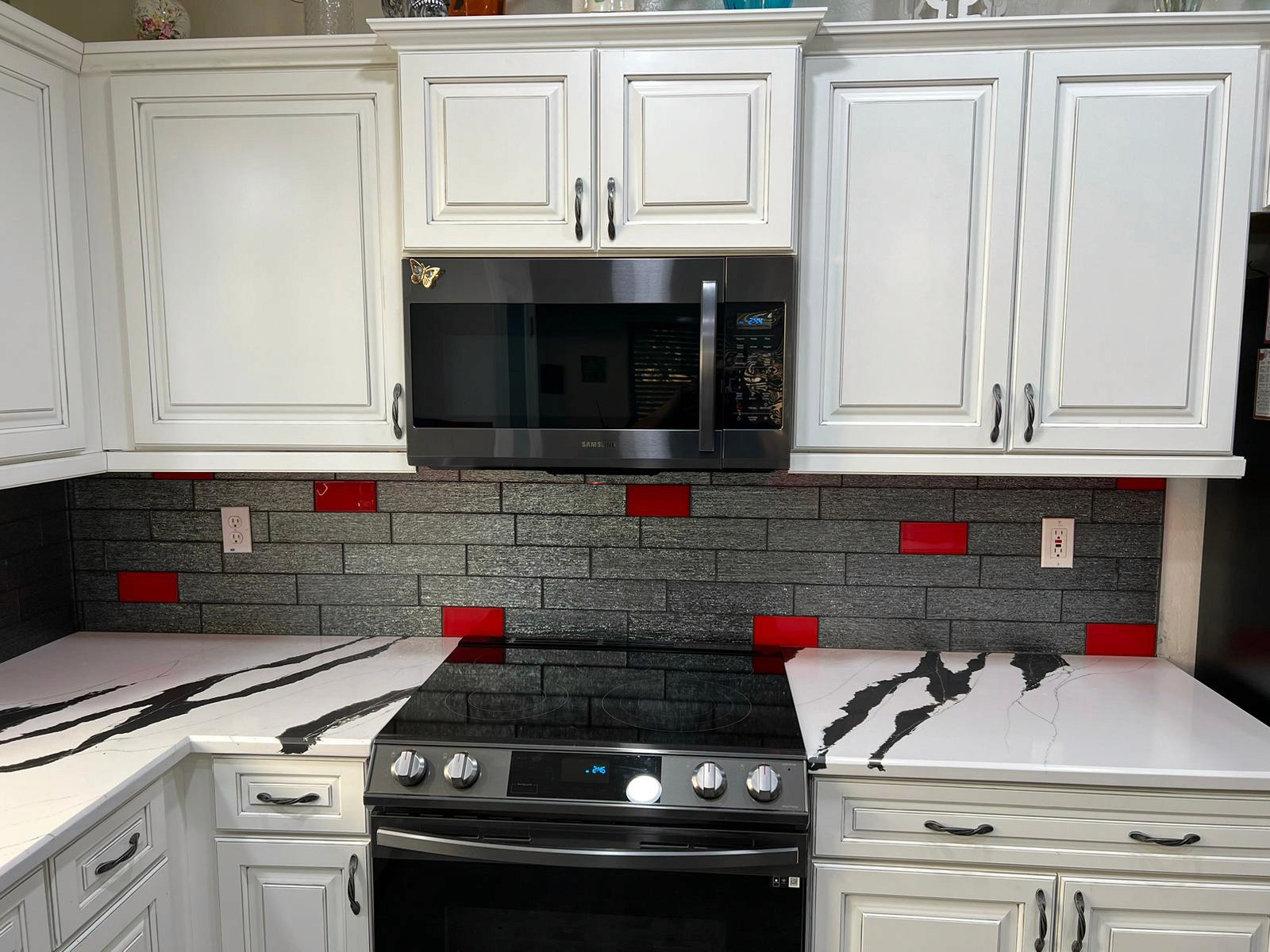 Modern kitchen with white cabinets, a black stovetop, and a backsplash featuring gray tiles with red accents.