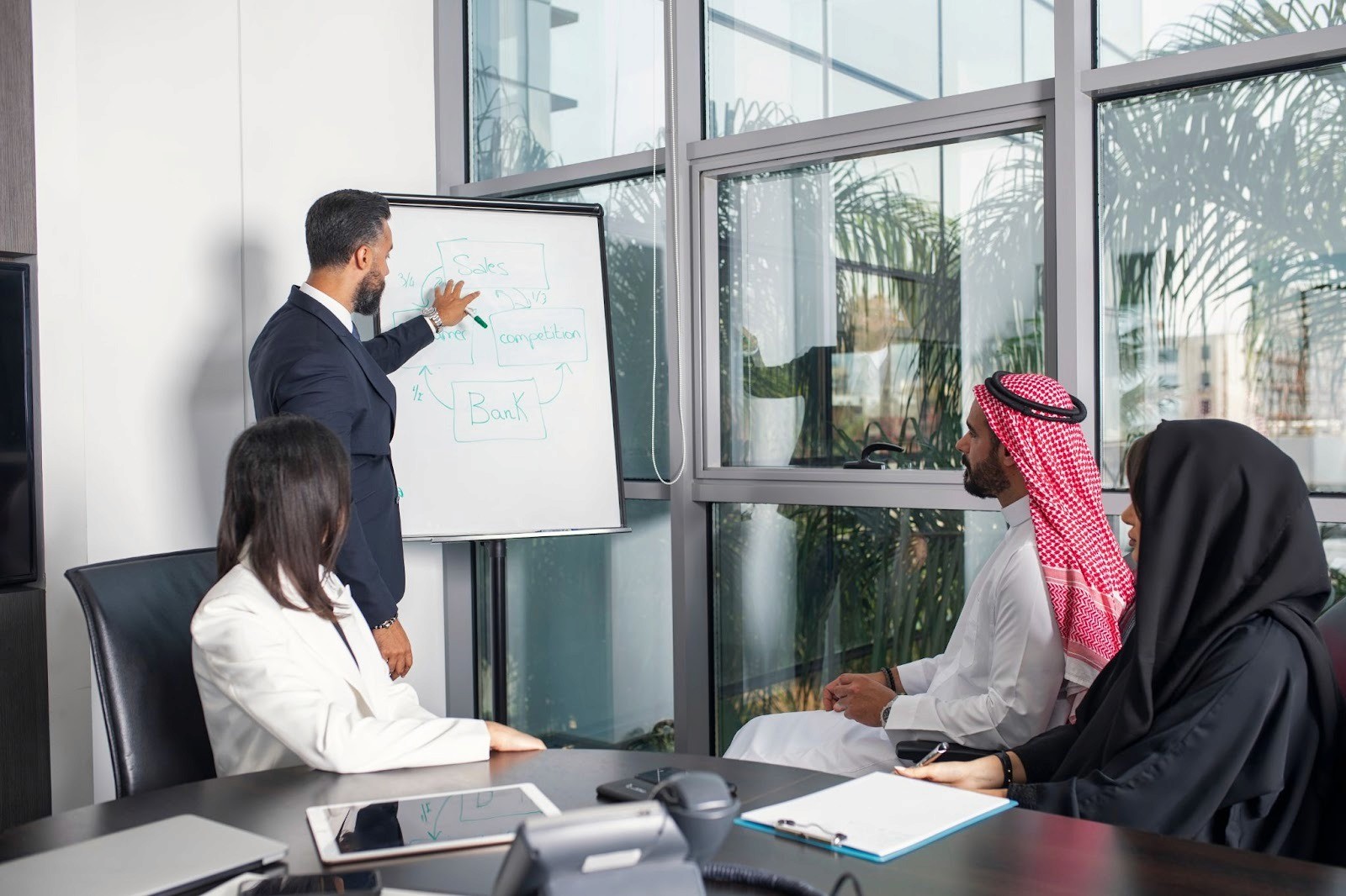 A group of multicultural employees in the UAE participating in a brainstorming session around a flip chart, collaborating in a modern office setting.