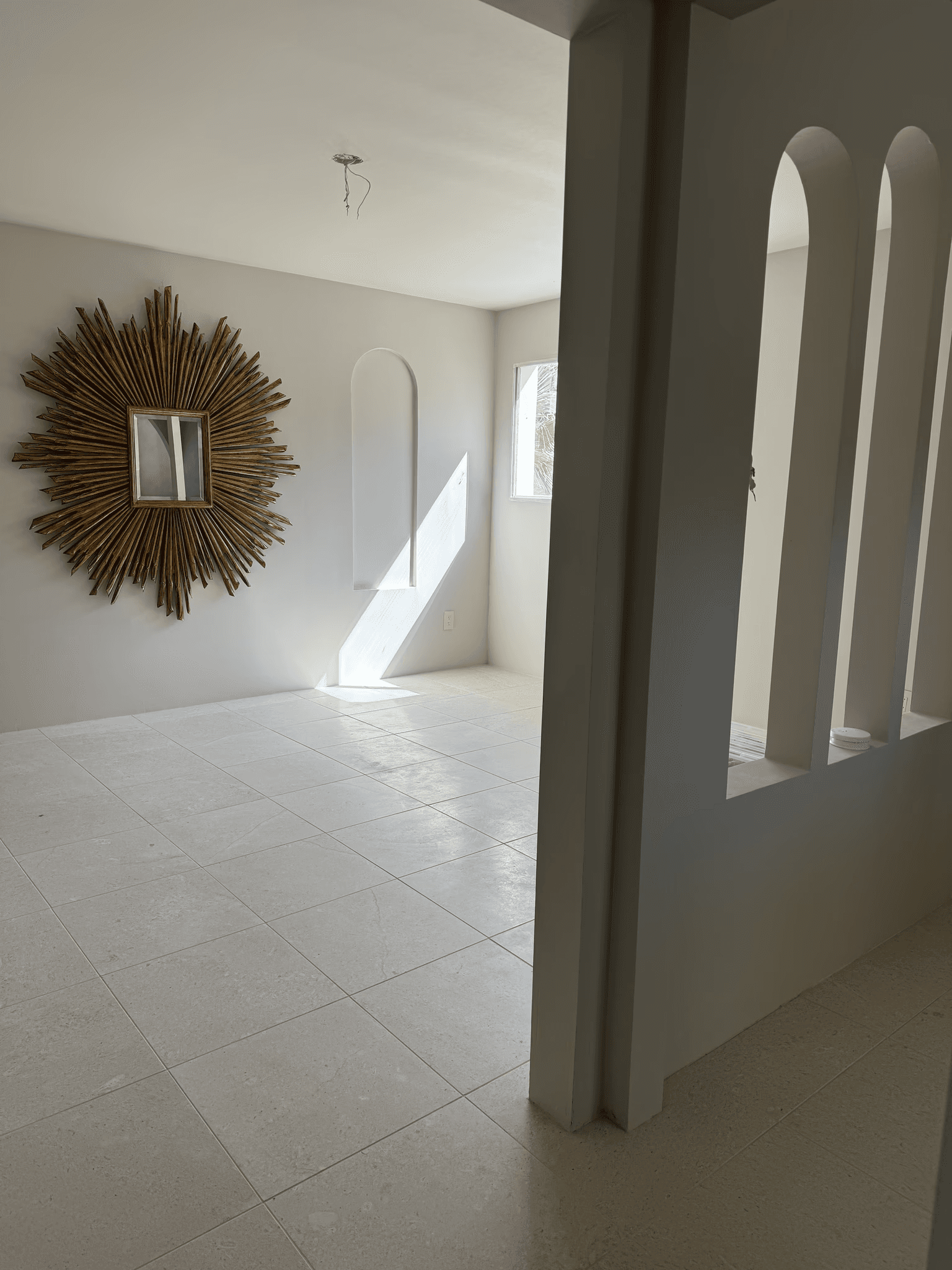 Modern living room with decorative sunburst mirror, arched wall cutouts, and large windows in a new home.