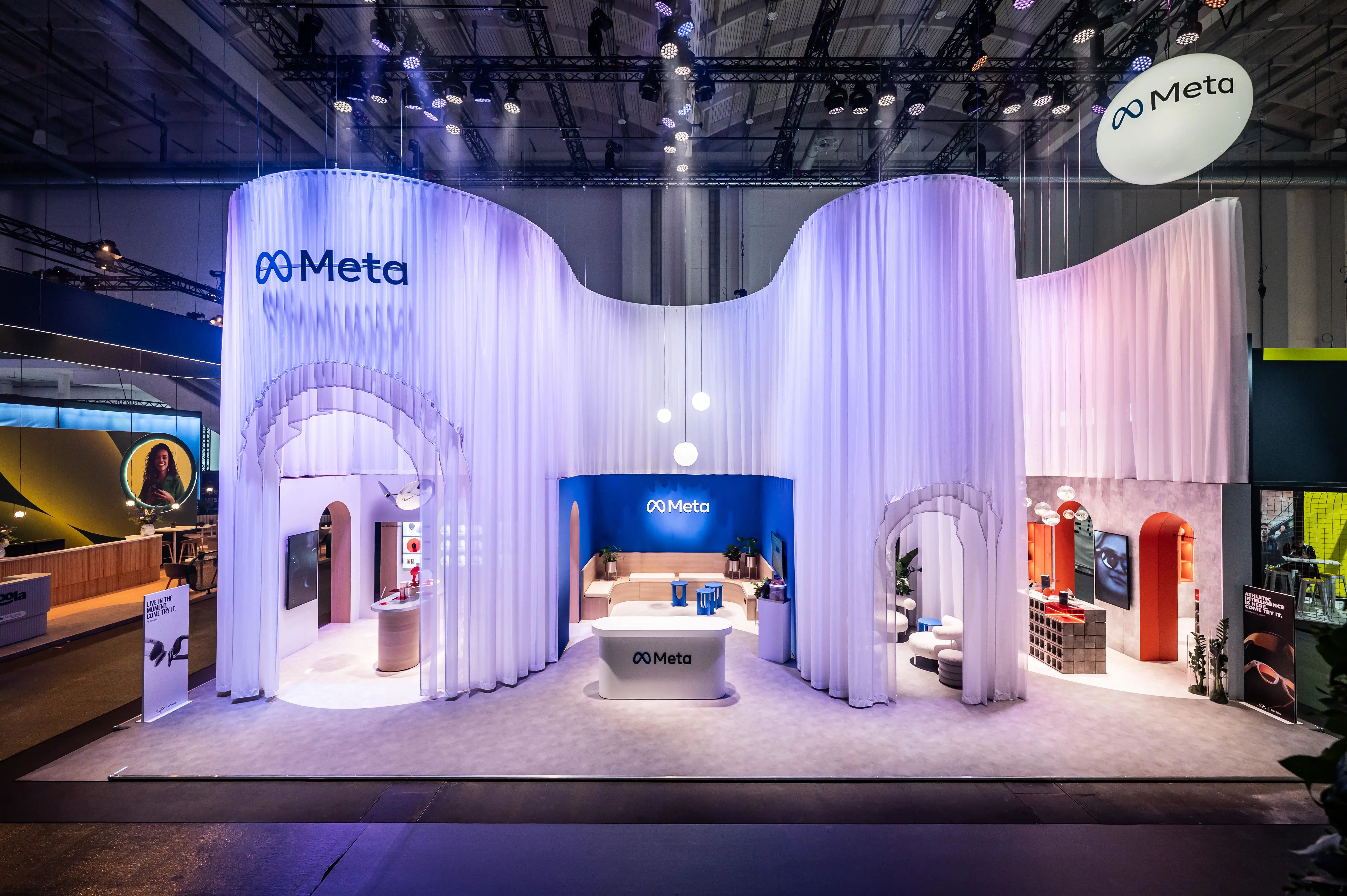 Full view of the Meta booth with flowing white curtain facade, arched openings and floating logo sign.