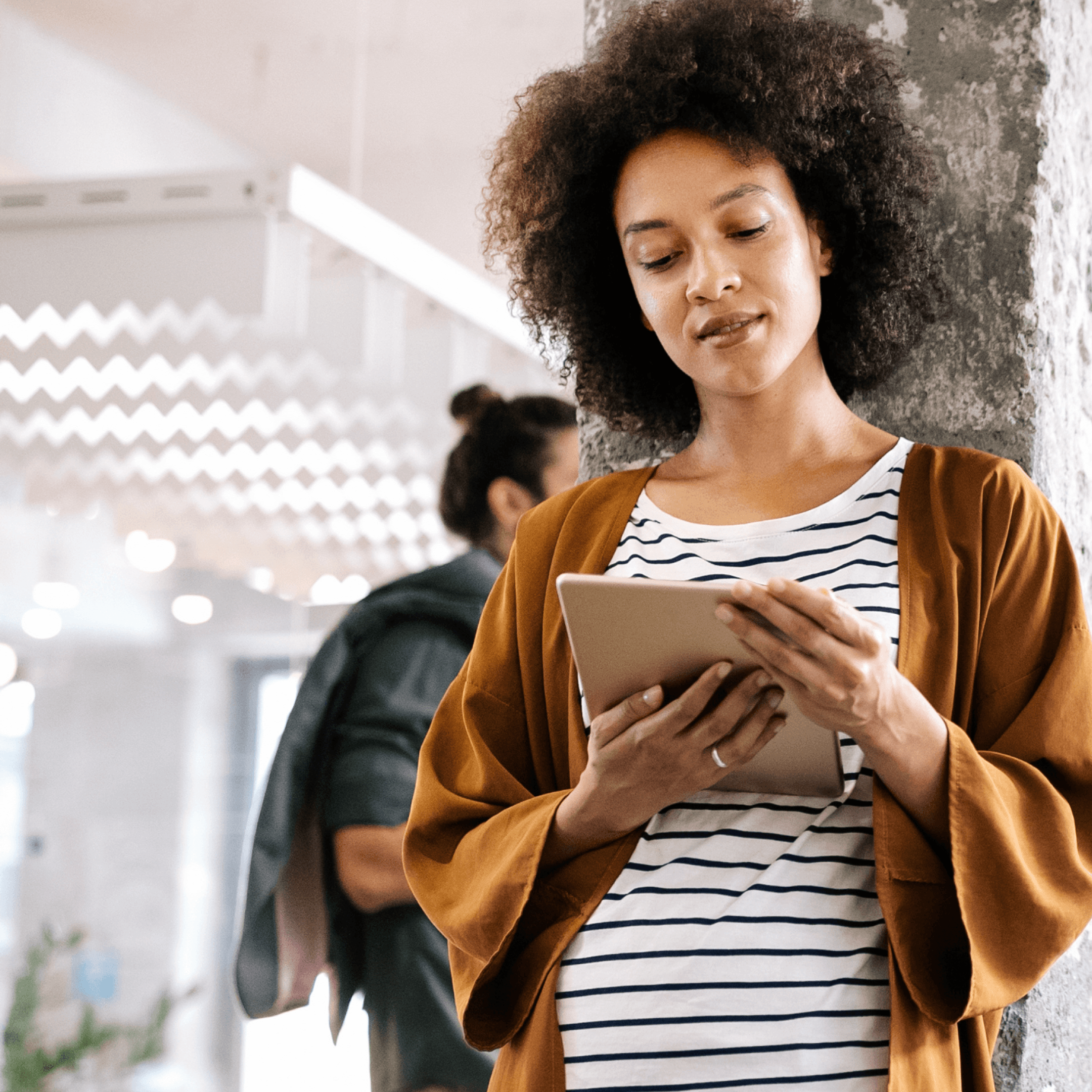 Vrouw met krullend haar, gekleed in een gestreept shirt en een bruine cardigan, bekijkt een tablet met informatie over RI&E dossieracties.