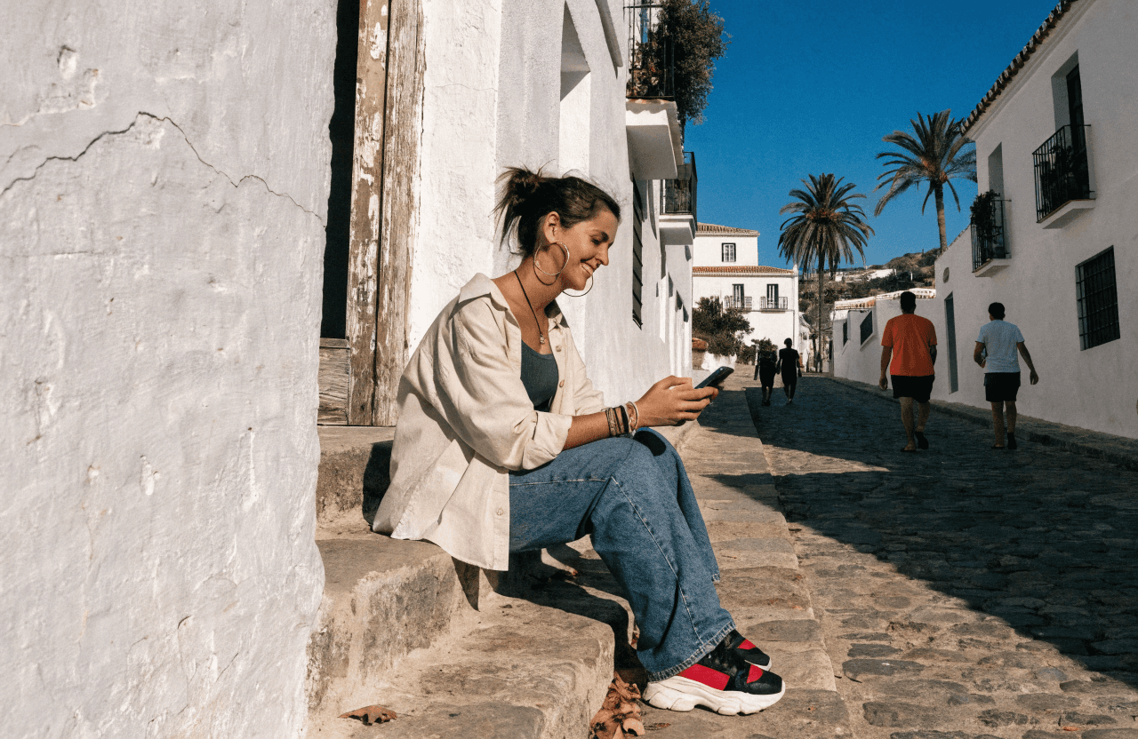 Mujer usando su móvil sentada en una calle de un pueblo blanco de la Costa del Sol