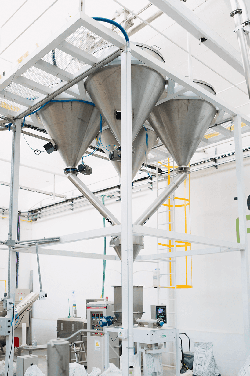 Industrial stainless steel hopper system above packaging equipment in a food processing facility.