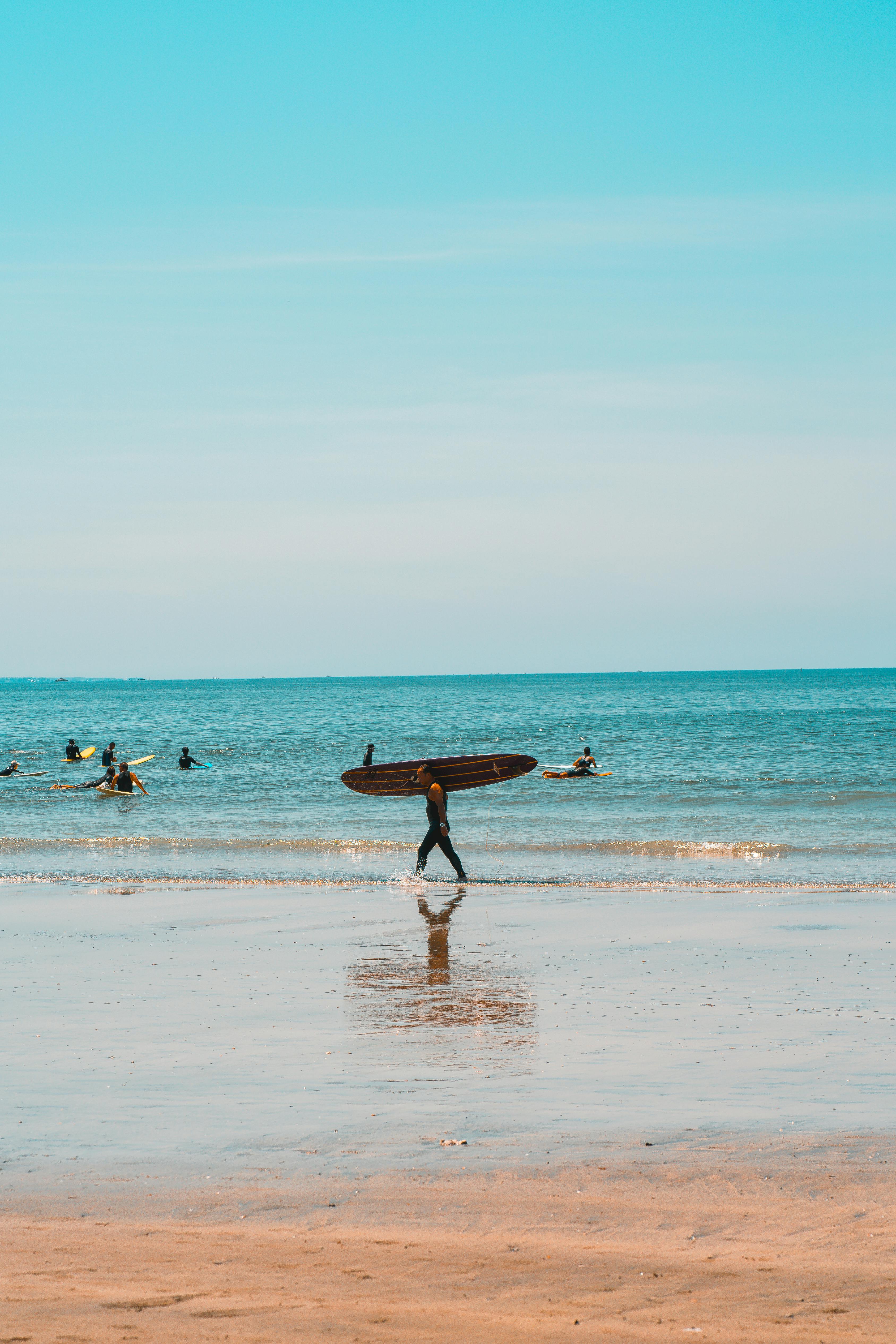 Man carrying surfboard on beach – surfboard rental in japan.