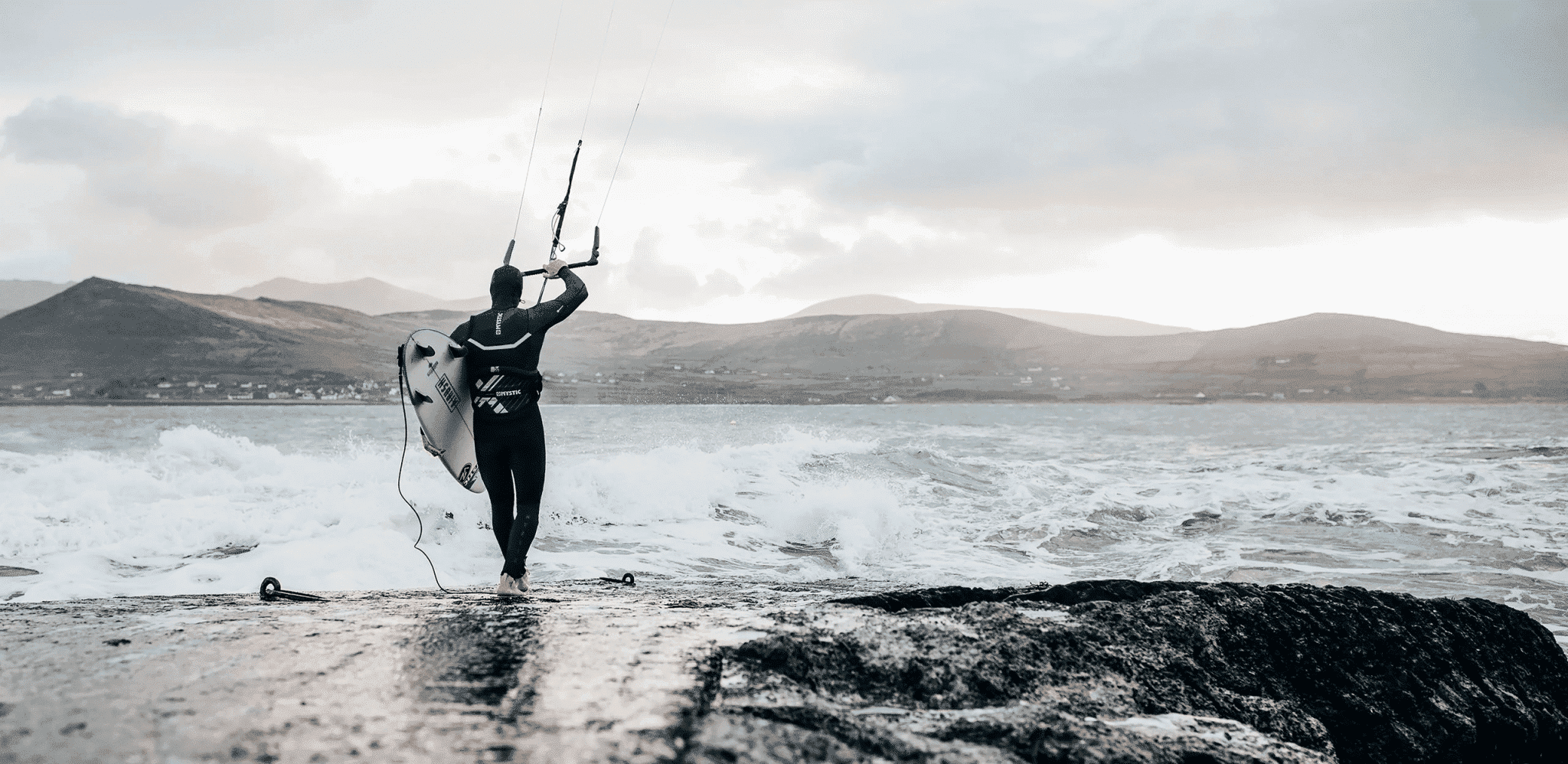 Kitesurfer with board and kite bar walking into rough sea, for the North Actionsports Group middleware case