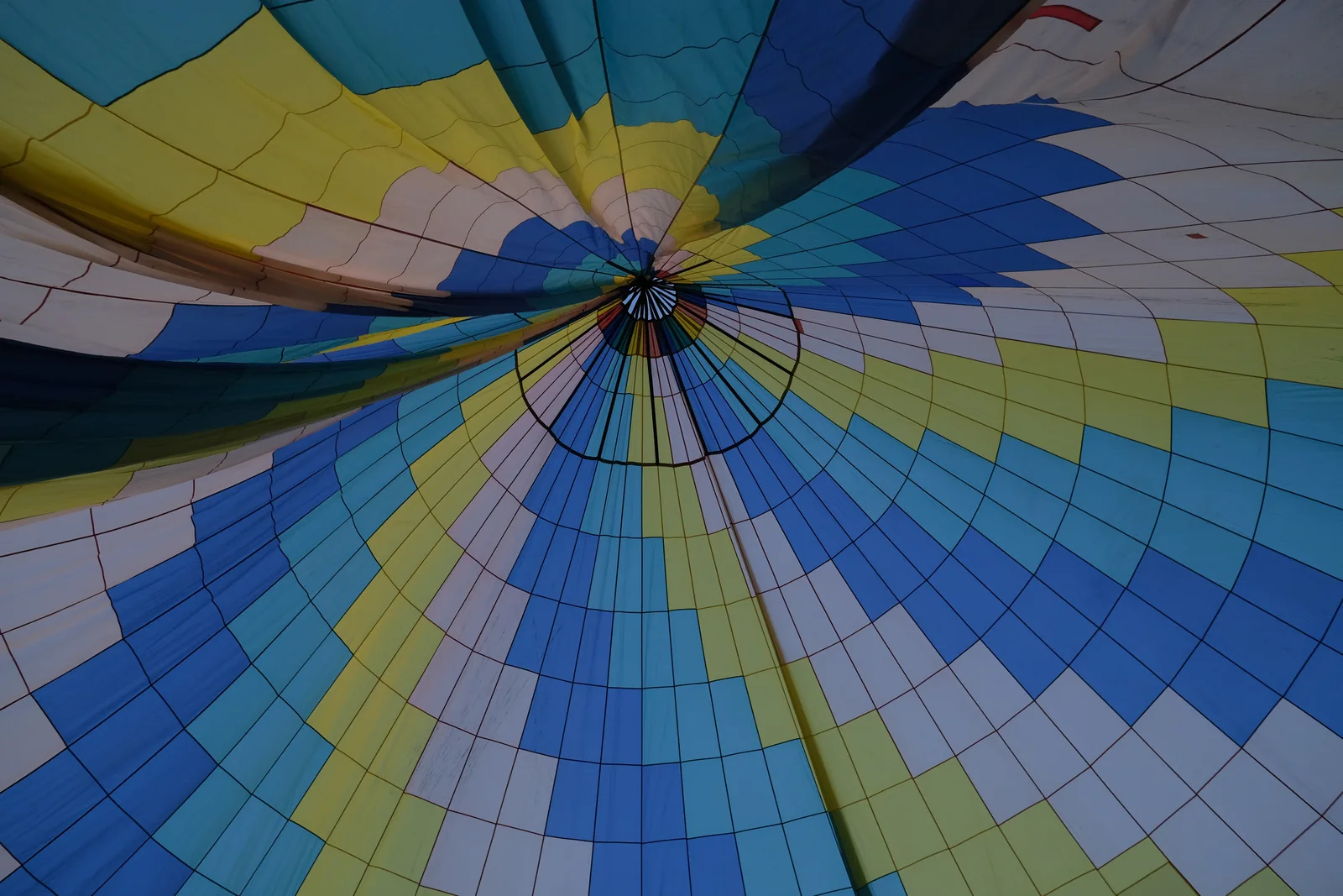 Blick von unten in die blau-gelbe Hülle eines Heißluftballons.