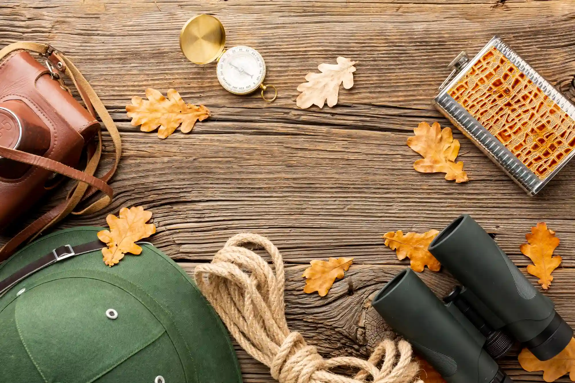 Autumn hiking gear: compass, binoculars, flask, rope, hat, leaves.