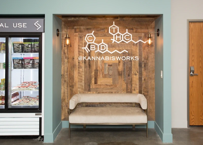 Kannabis Works accent wall with neon sign and wooden bench in a relaxed setting.