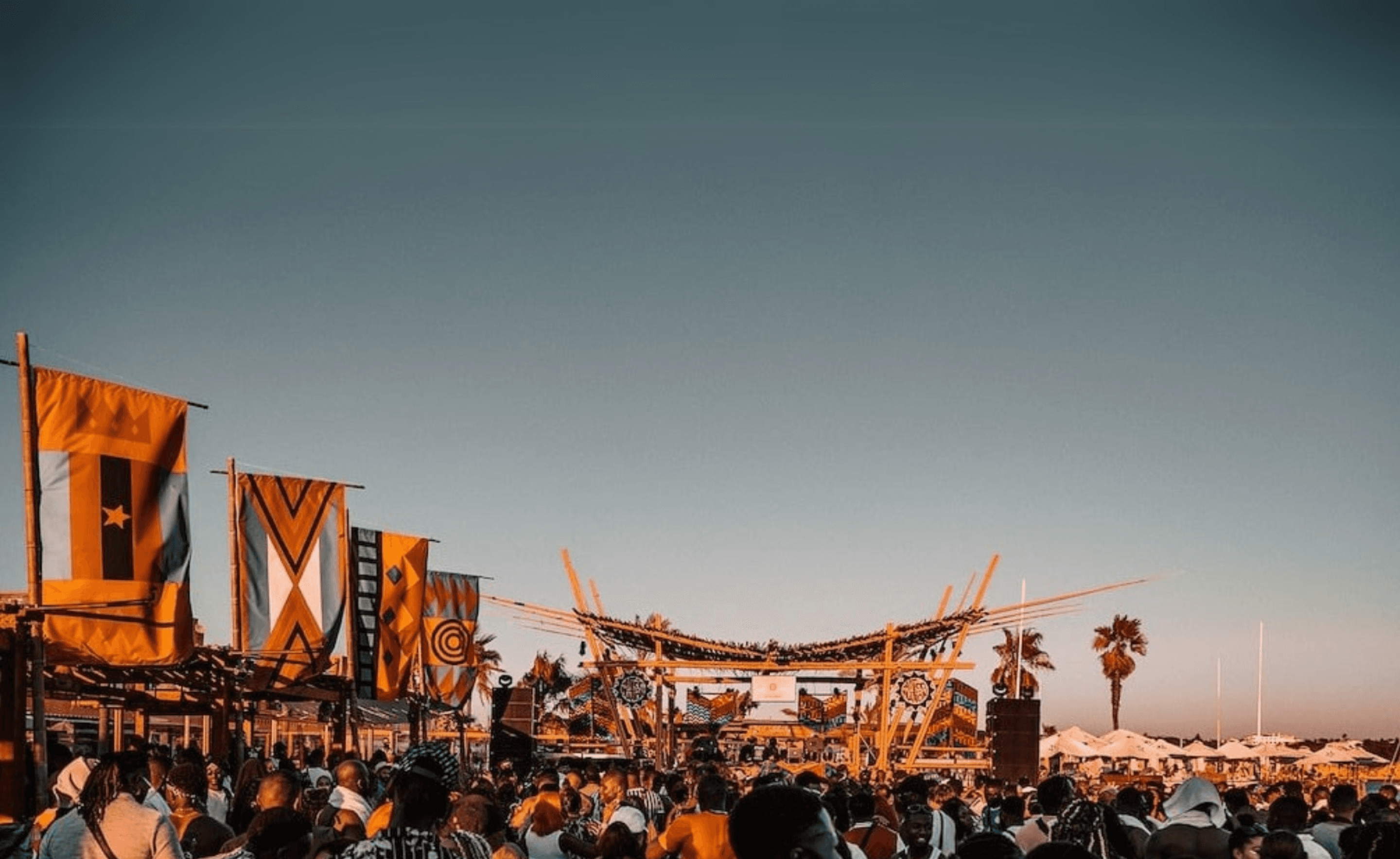 Large crowd enjoying a vibrant outdoor experiential event with an elaborate stage setup and cultural decorations.