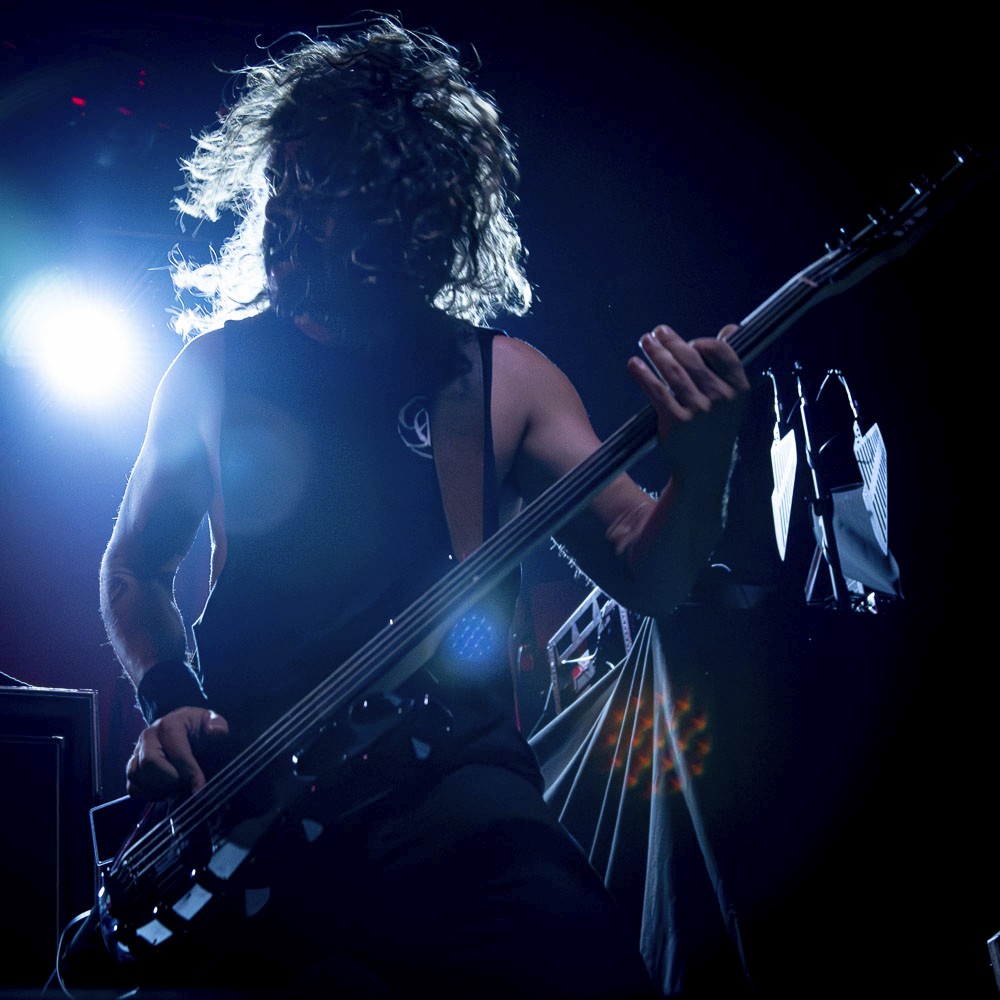 Live concert photography of a bassist performing on stage under moody blue and dramatic theatrical lighting.