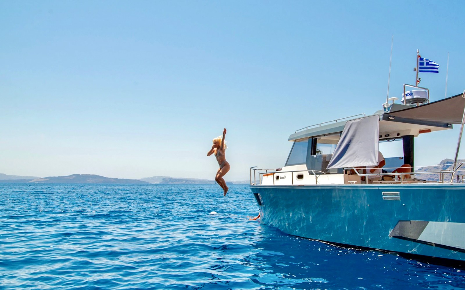 Person jumping off a catamaran into the Aegean Sea during a Santorini Caldera cruise.