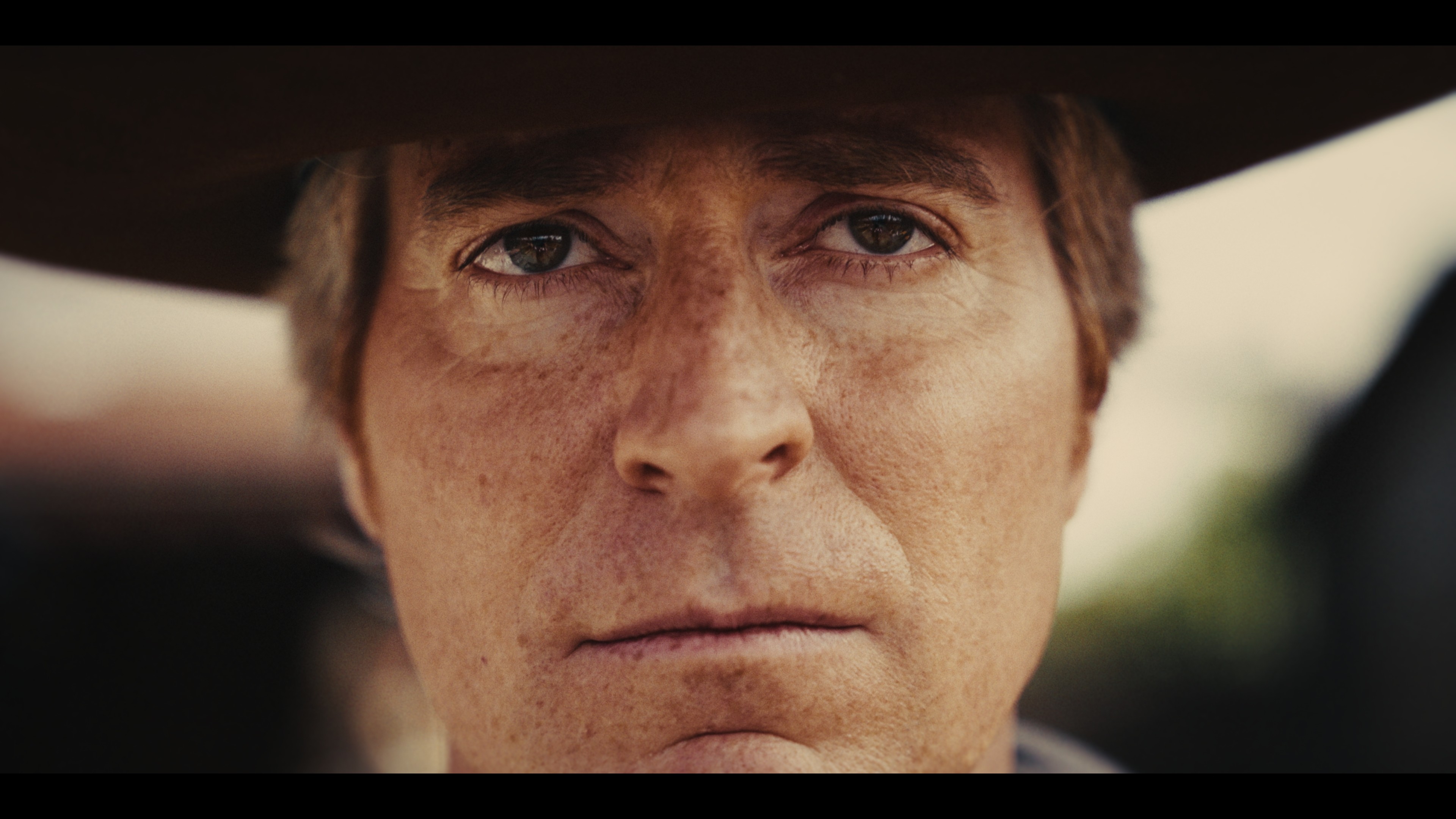 Screenshot form a Video. Man with Cowboyhat staring into Camera.